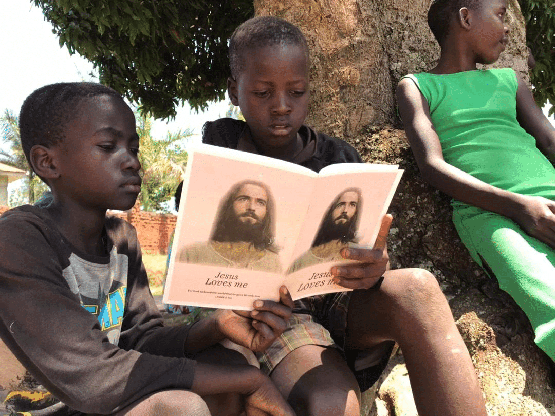 Boy reading an open gospel tract booklet with a portrait of Jesus beside another child