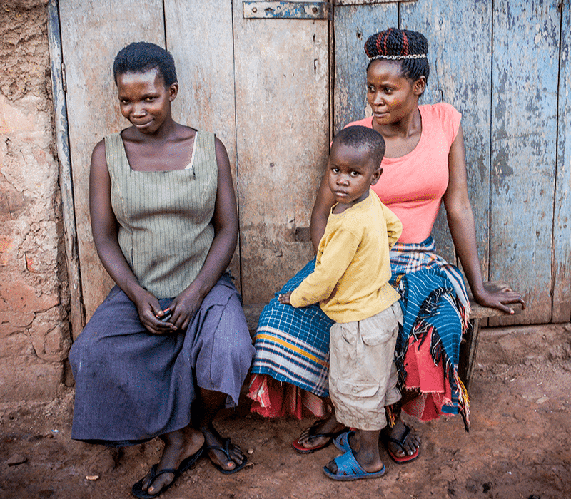 Two women and a young child pose together in front of a weathered blue wooden door of a mud-brick home.