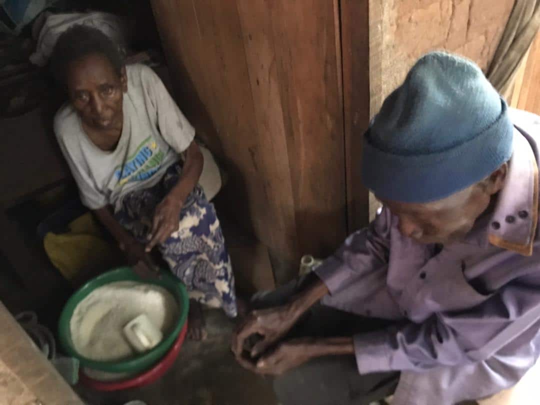 Two elderly women in dim indoor light, one holding a cooking pot, image blurred.