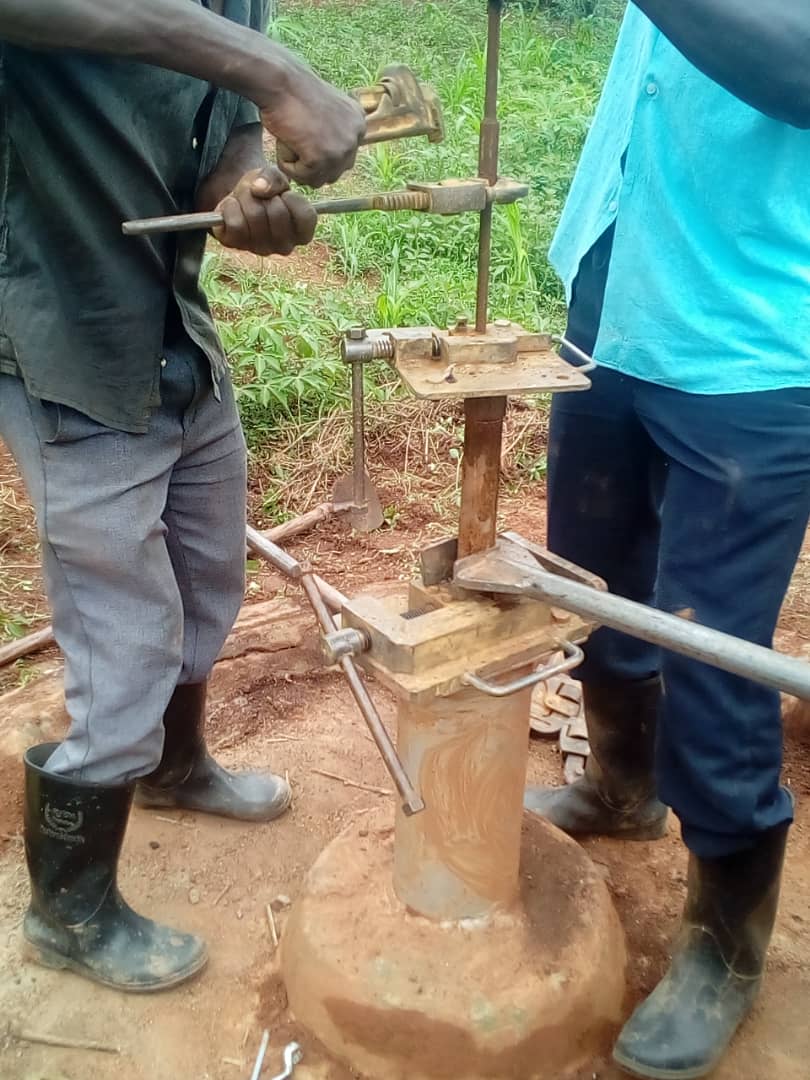 A man uses a wrench on the metal pump mechanism of a well repair site.