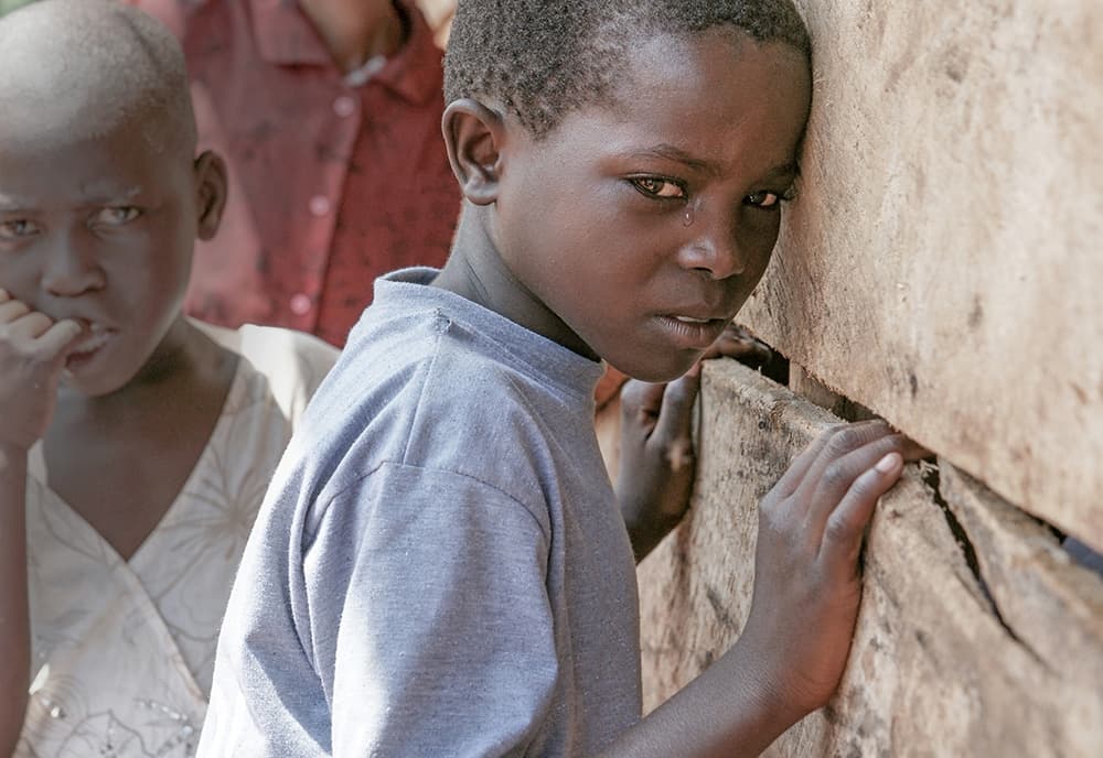 A boy stands outside a mud wall.