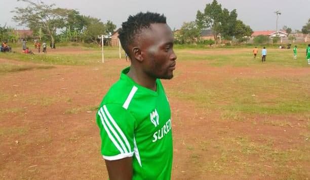 Young man in a green soccer jersey stands on an outdoor sports field.