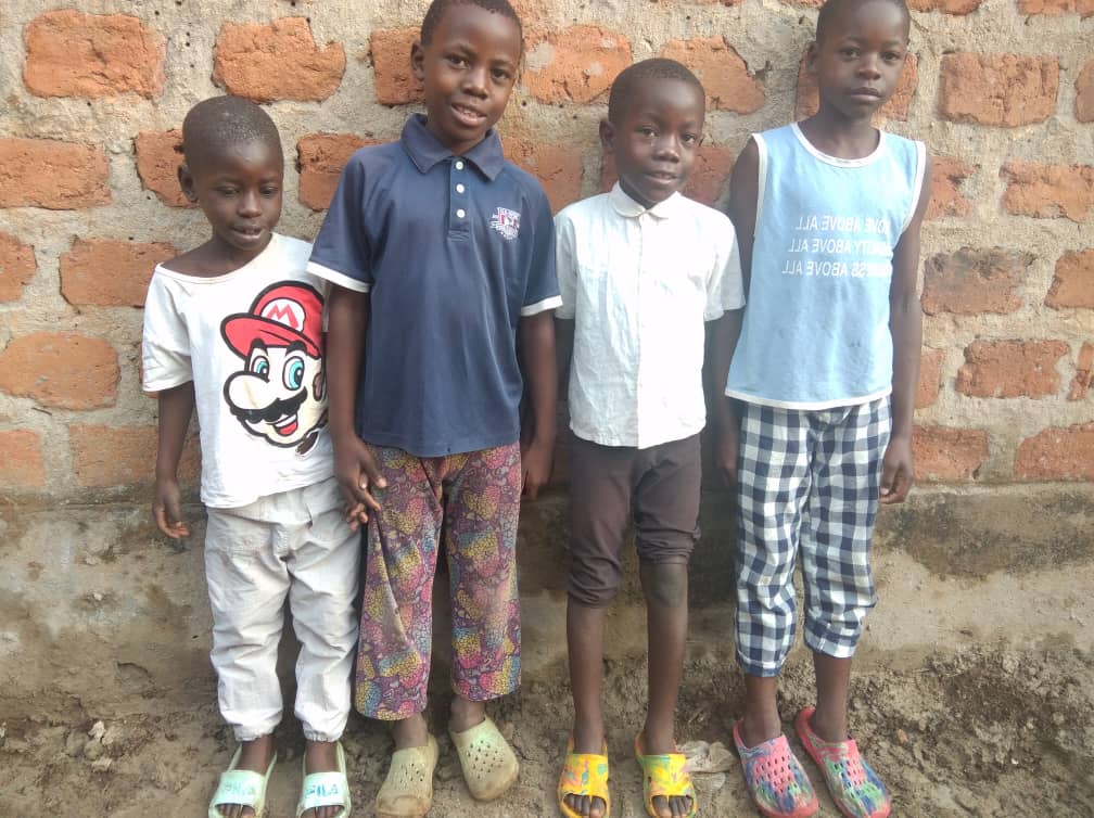 Four orphan boys stand together in matching outfits outside a brick wall for a group photo.