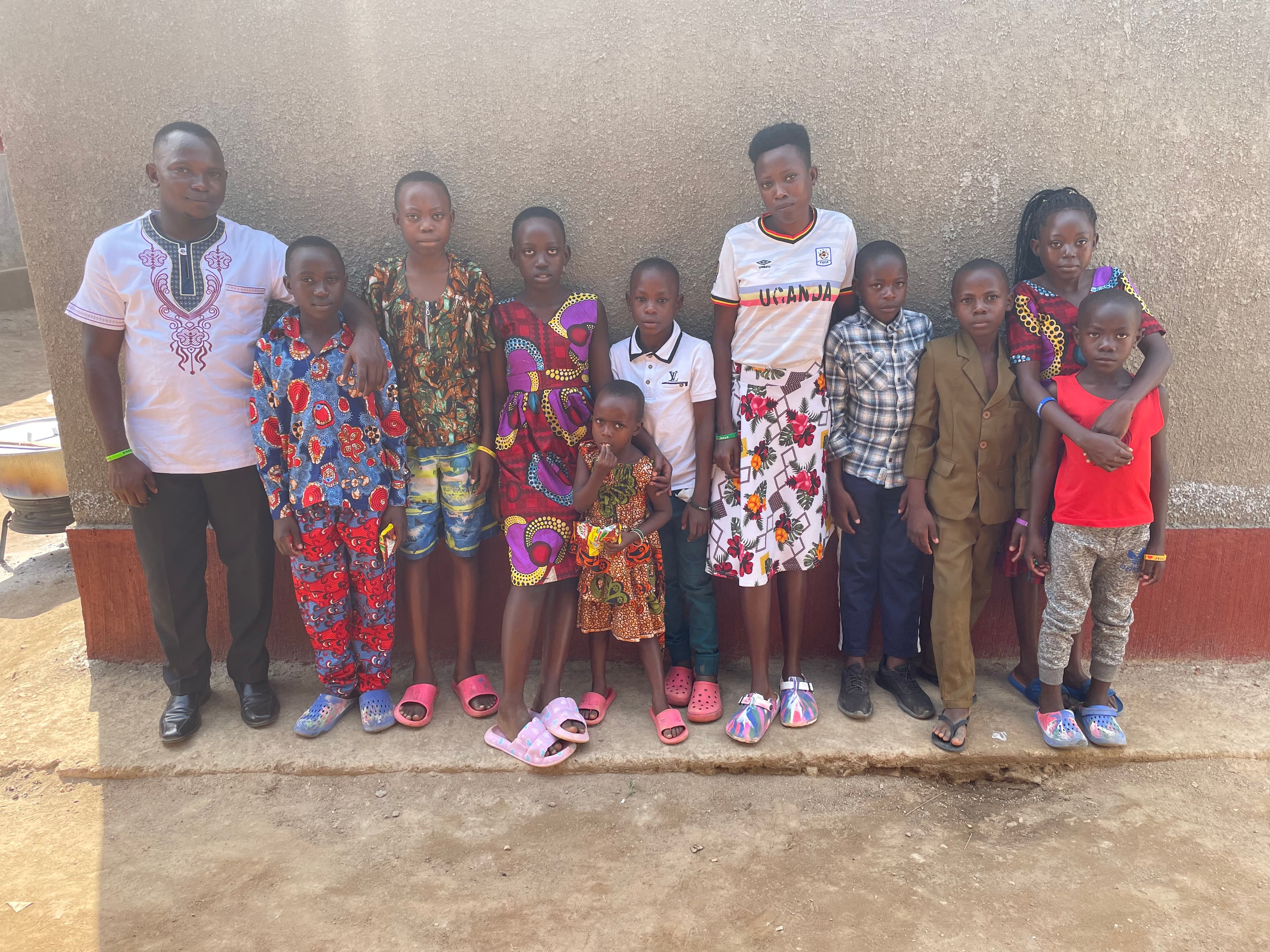 A group of women and children in patterned dresses pose together outside a brick building.