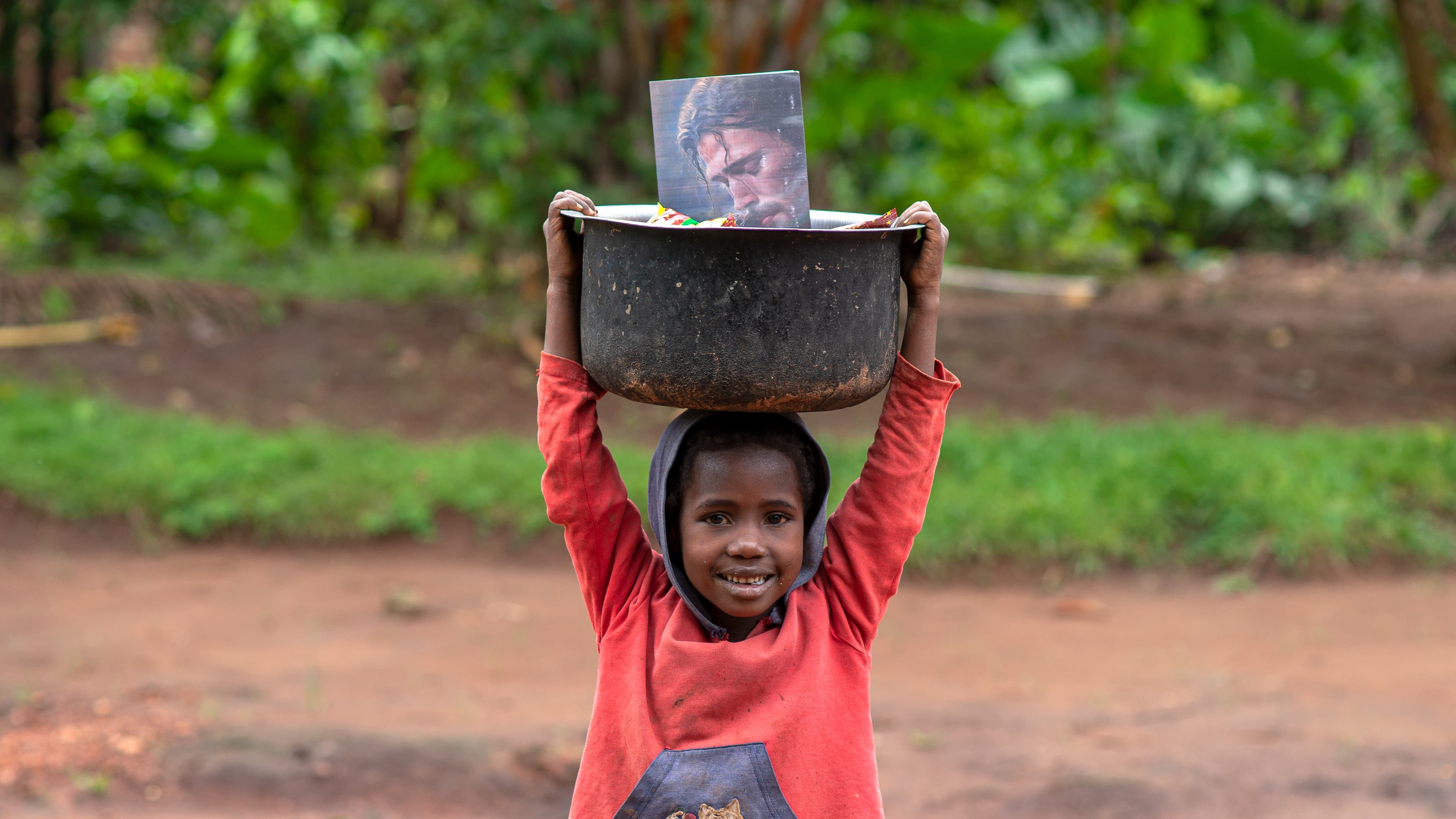 A girl carries a black cooking pot on her head.