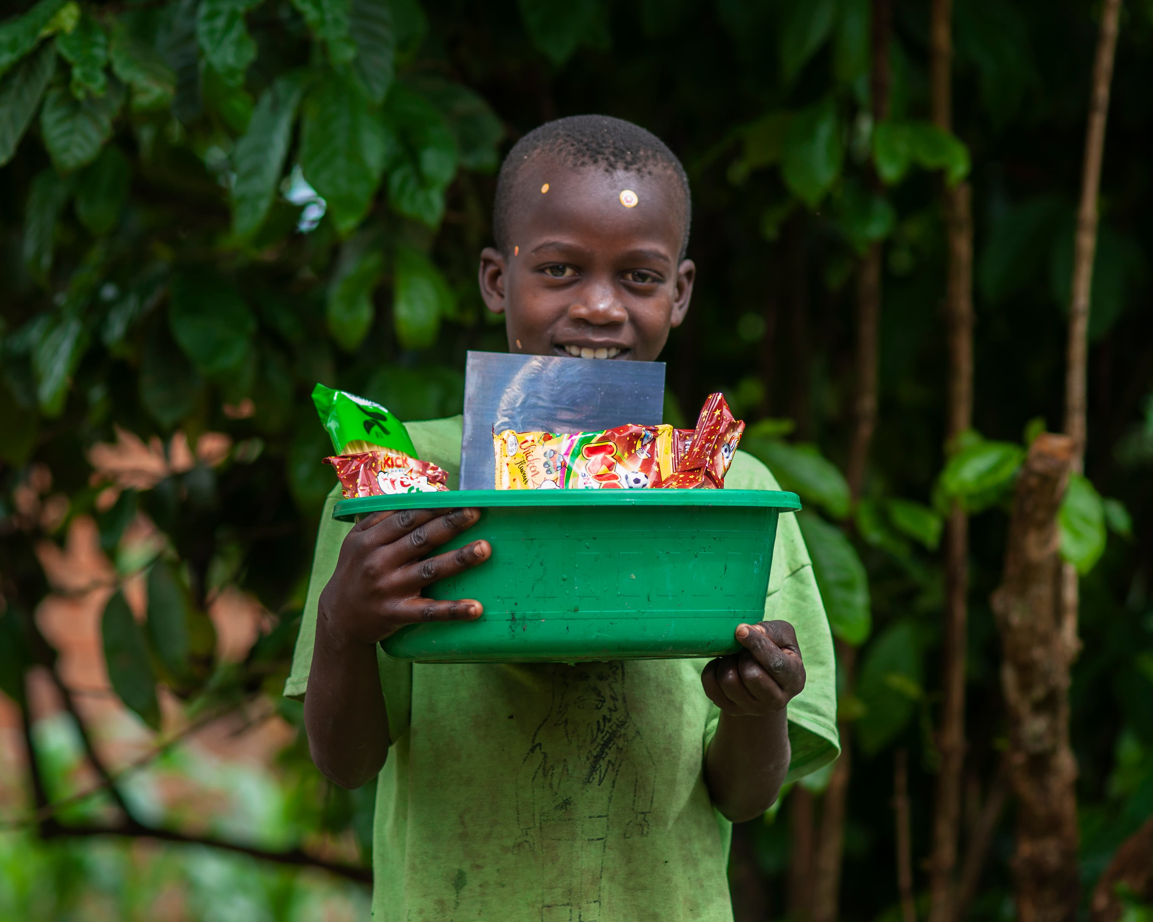 A boy smiles while holding a green box containing a photo card.