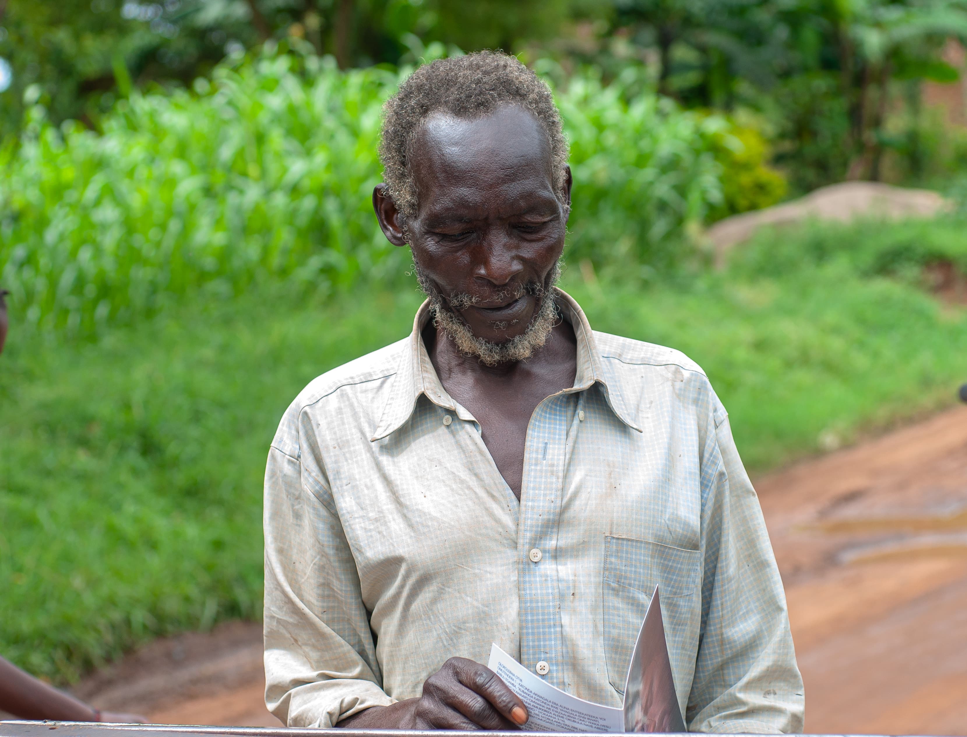 An elderly man stands outdoors holding a gospel booklet.