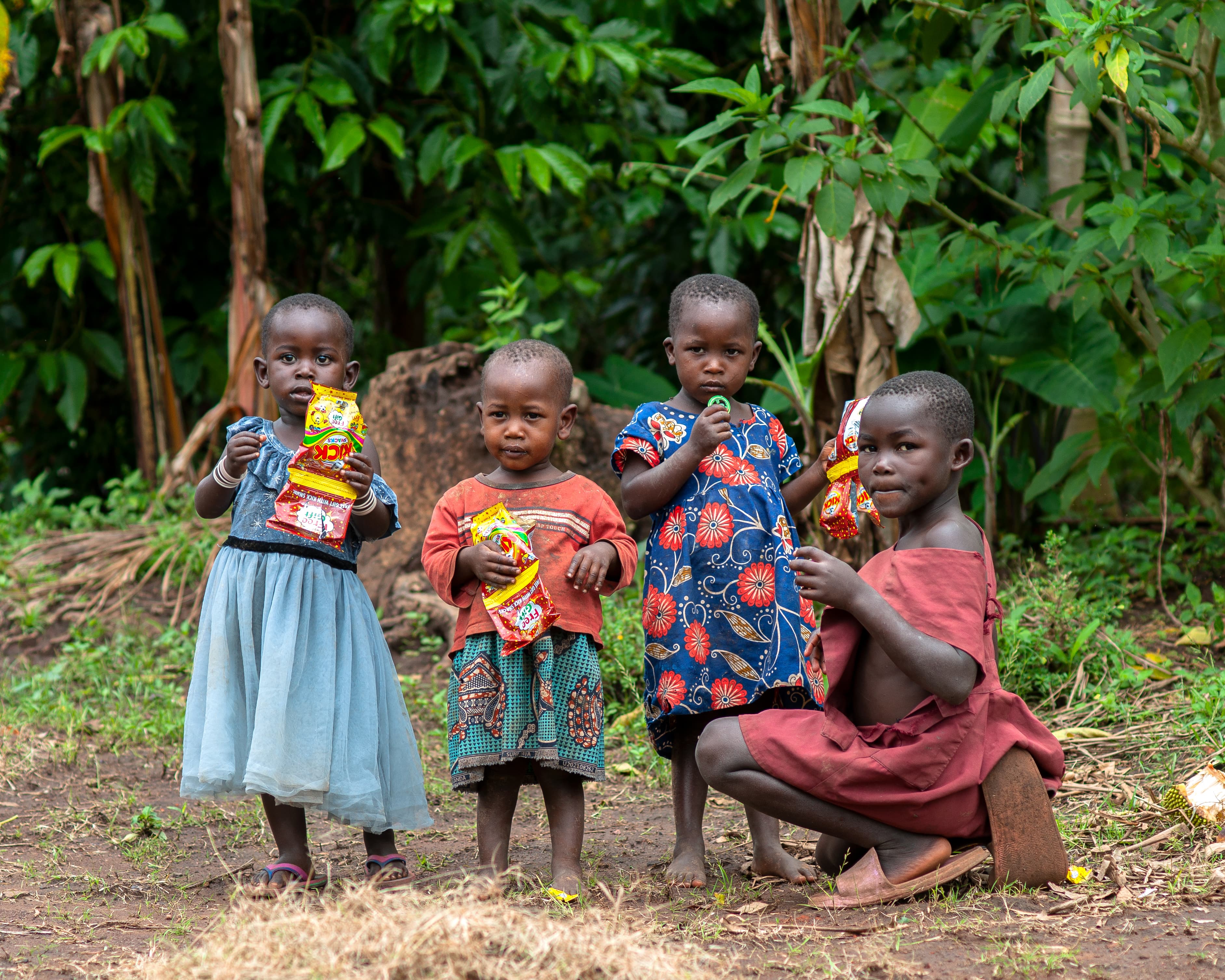 A group of children stand together outdoors, one crouching on the ground.