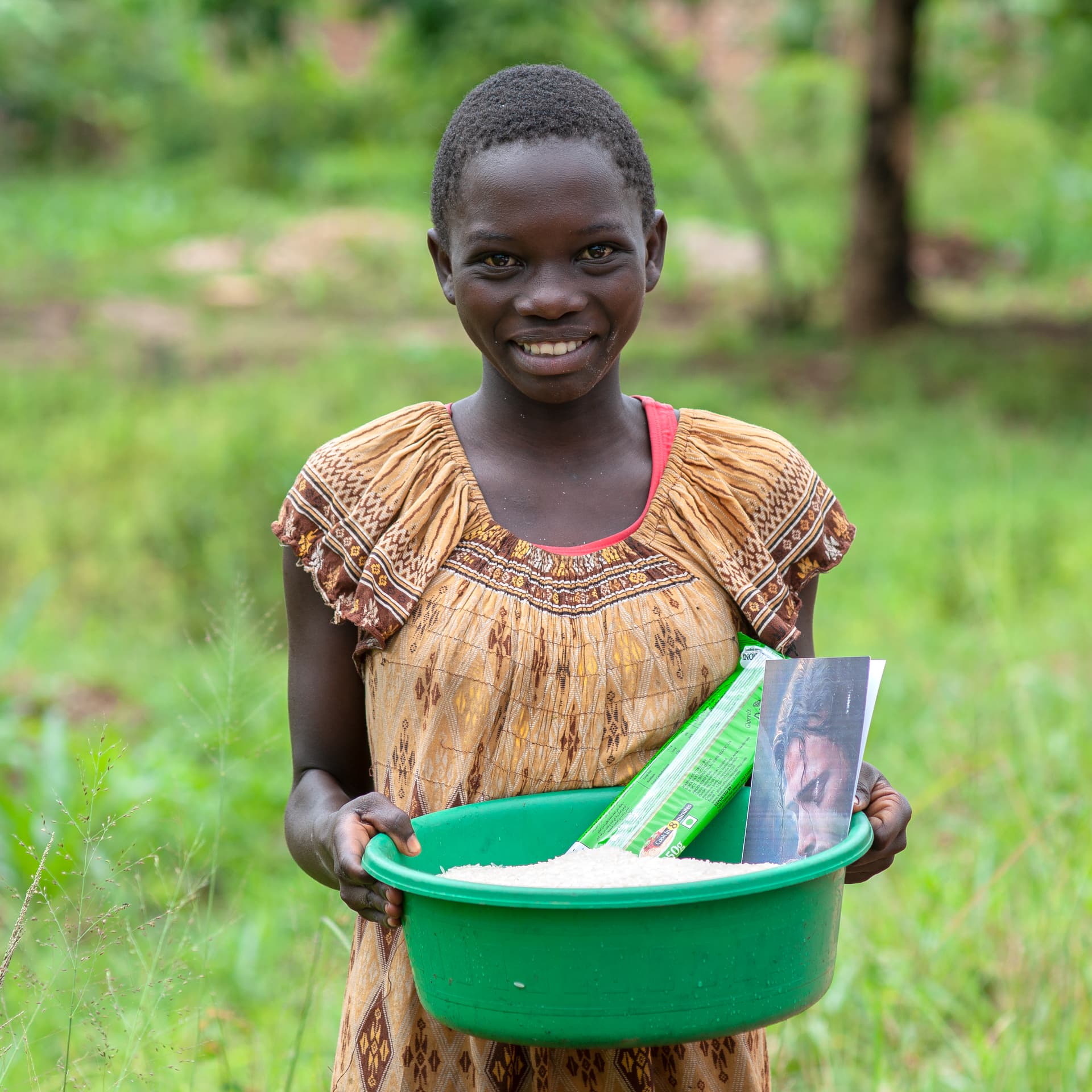 A girl smiles while holding a green bowl with a photo card inside.