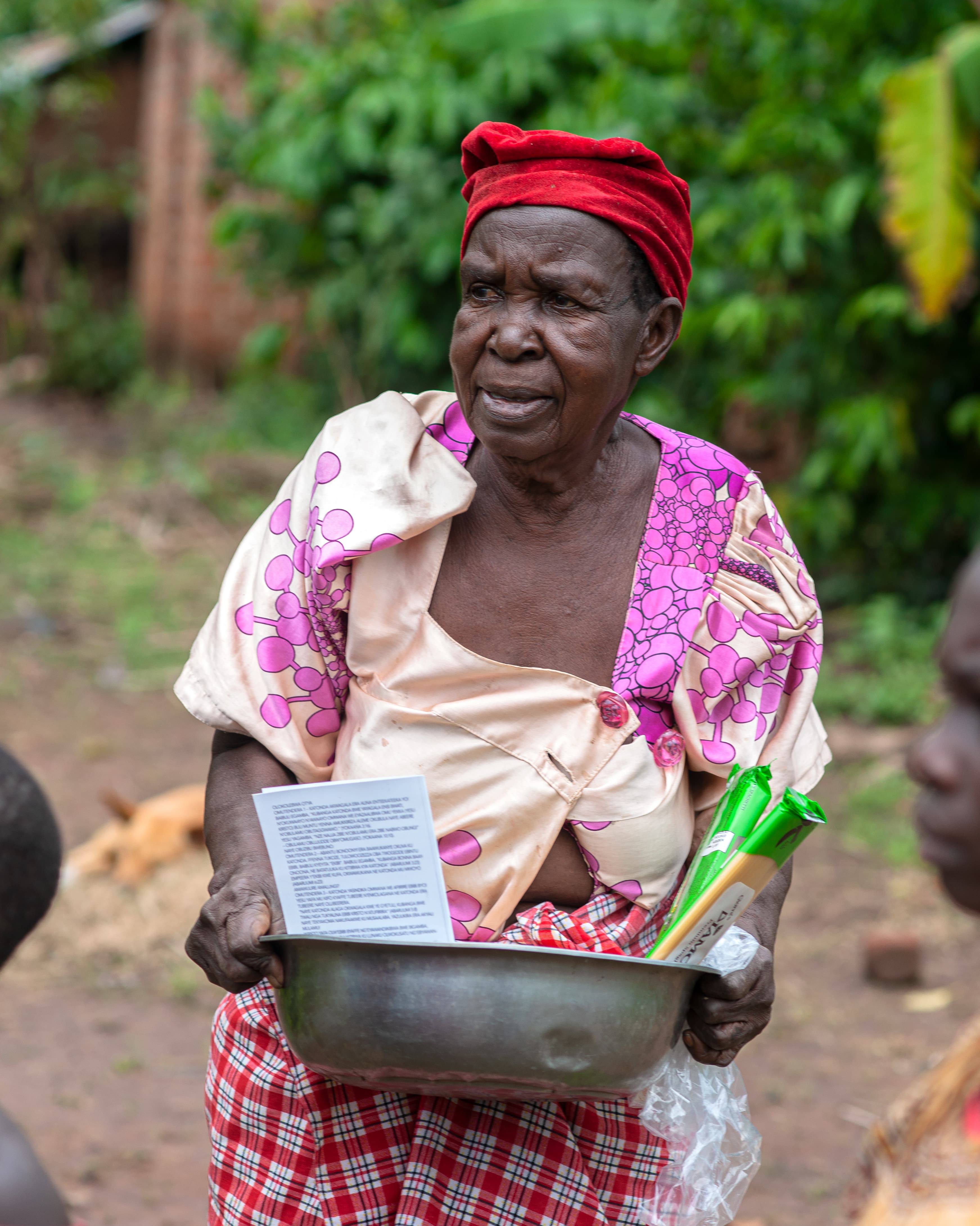 An elderly woman in pink holds a metal pot with a gospel booklet inside.