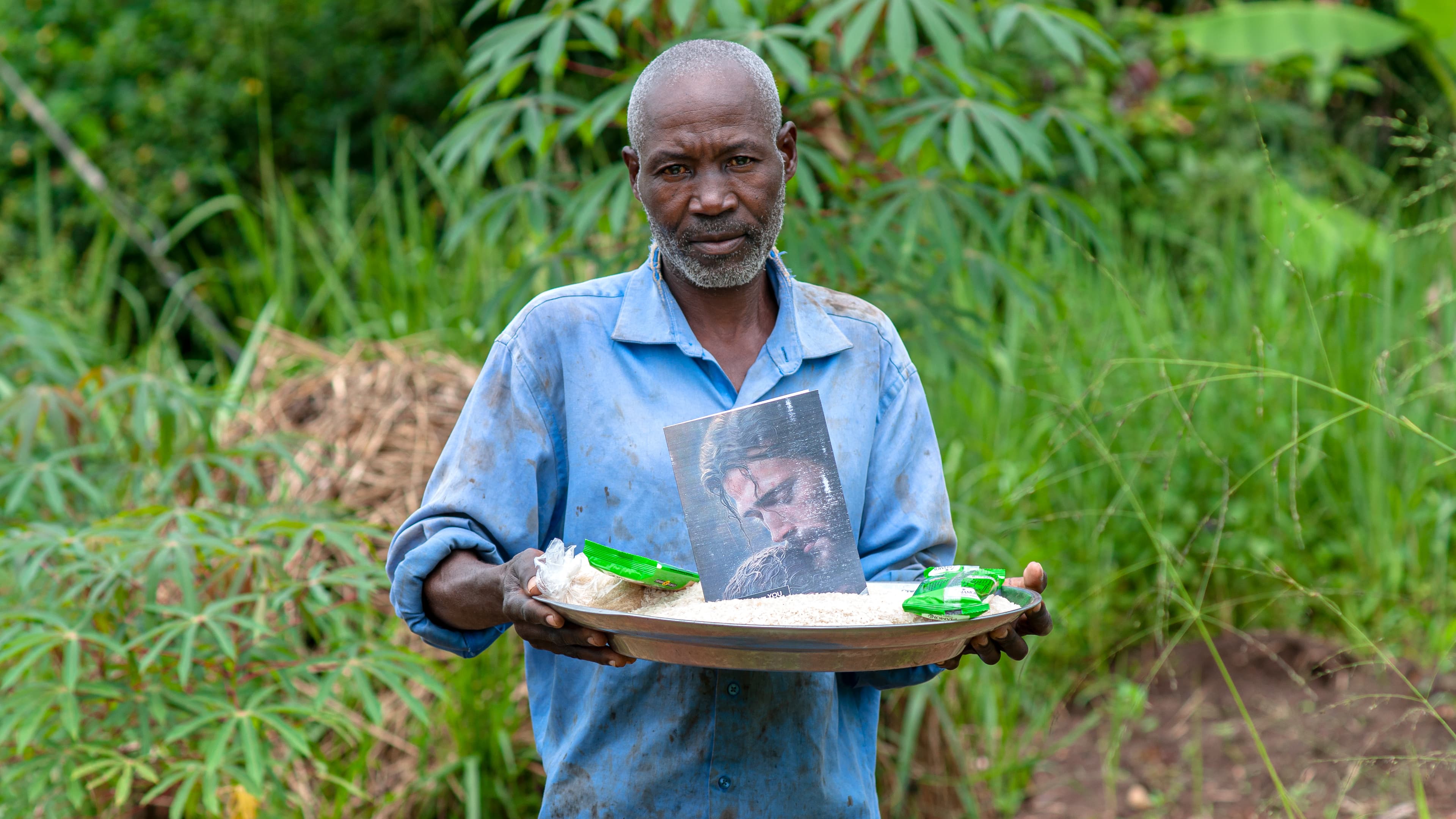 An elderly man in a blue shirt holds a plate with a photo card on it.