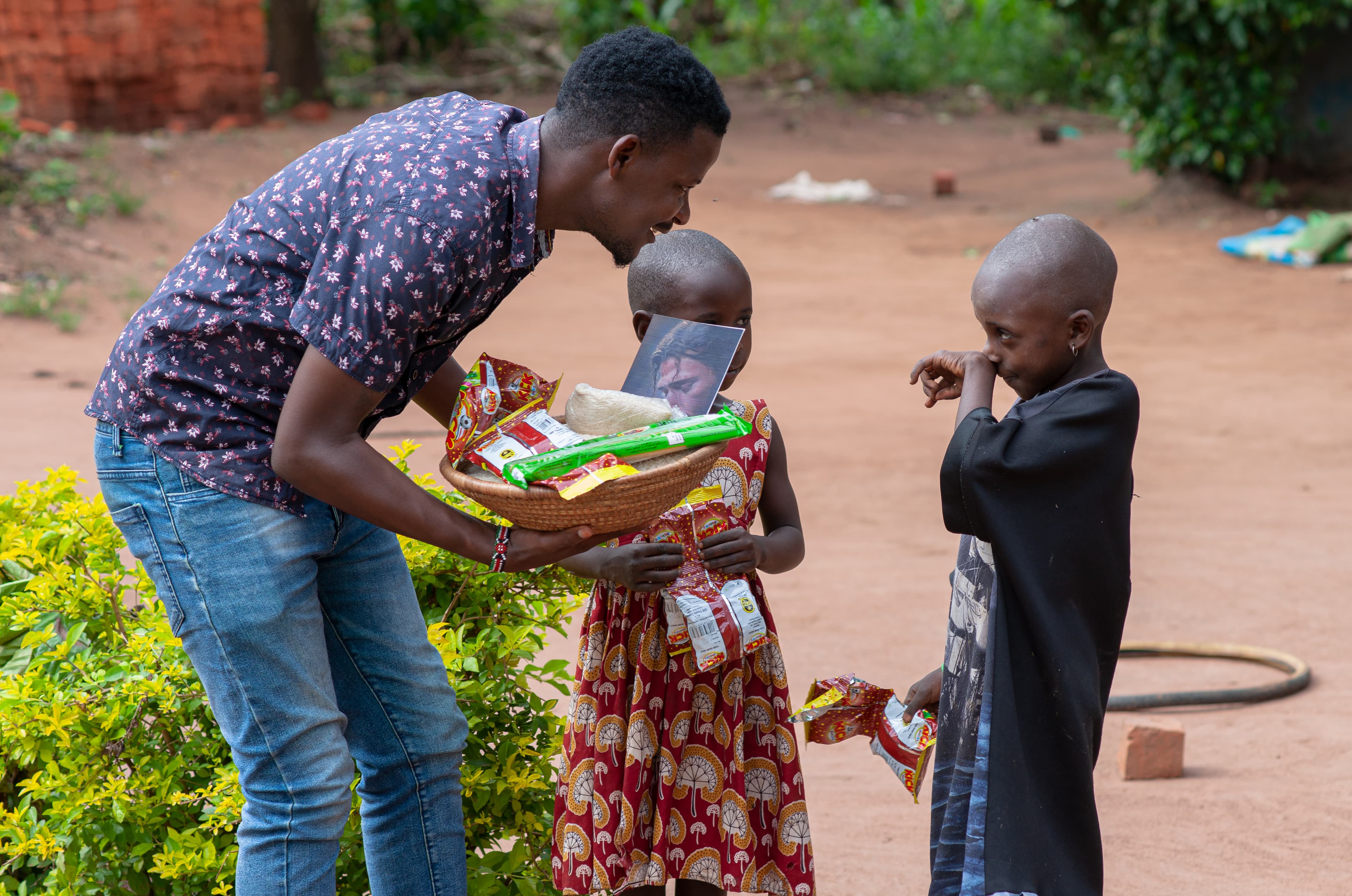 A JFM volunteer bends down to hand food packages to two young children in a village yard.