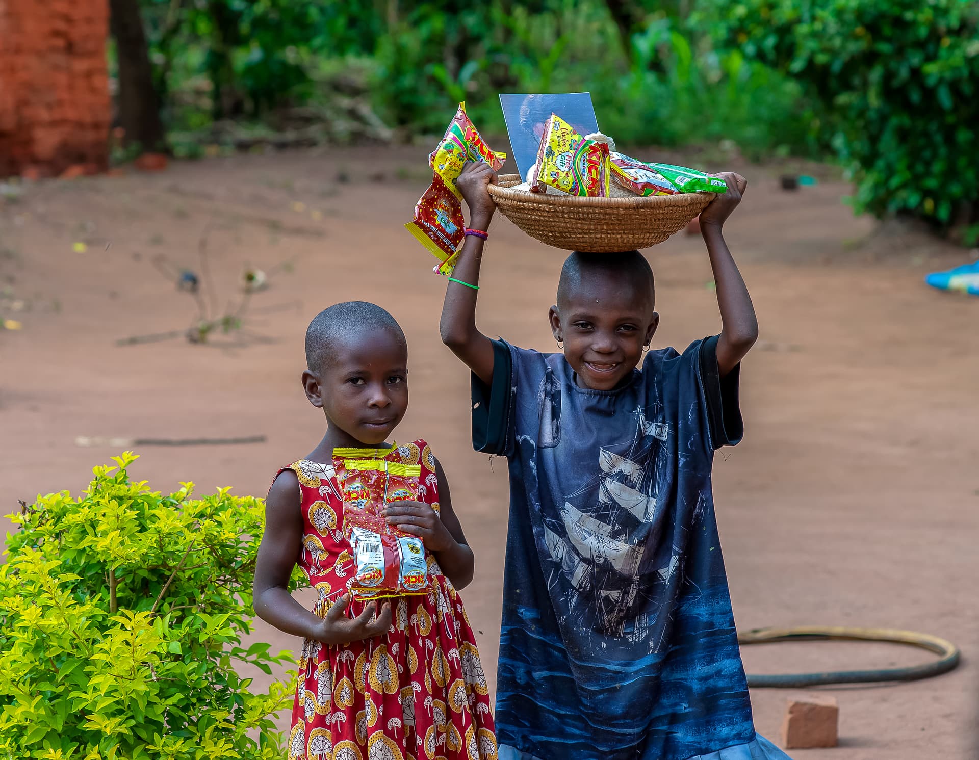 Two children carry food packages, one balancing a bowl of goods on her head.