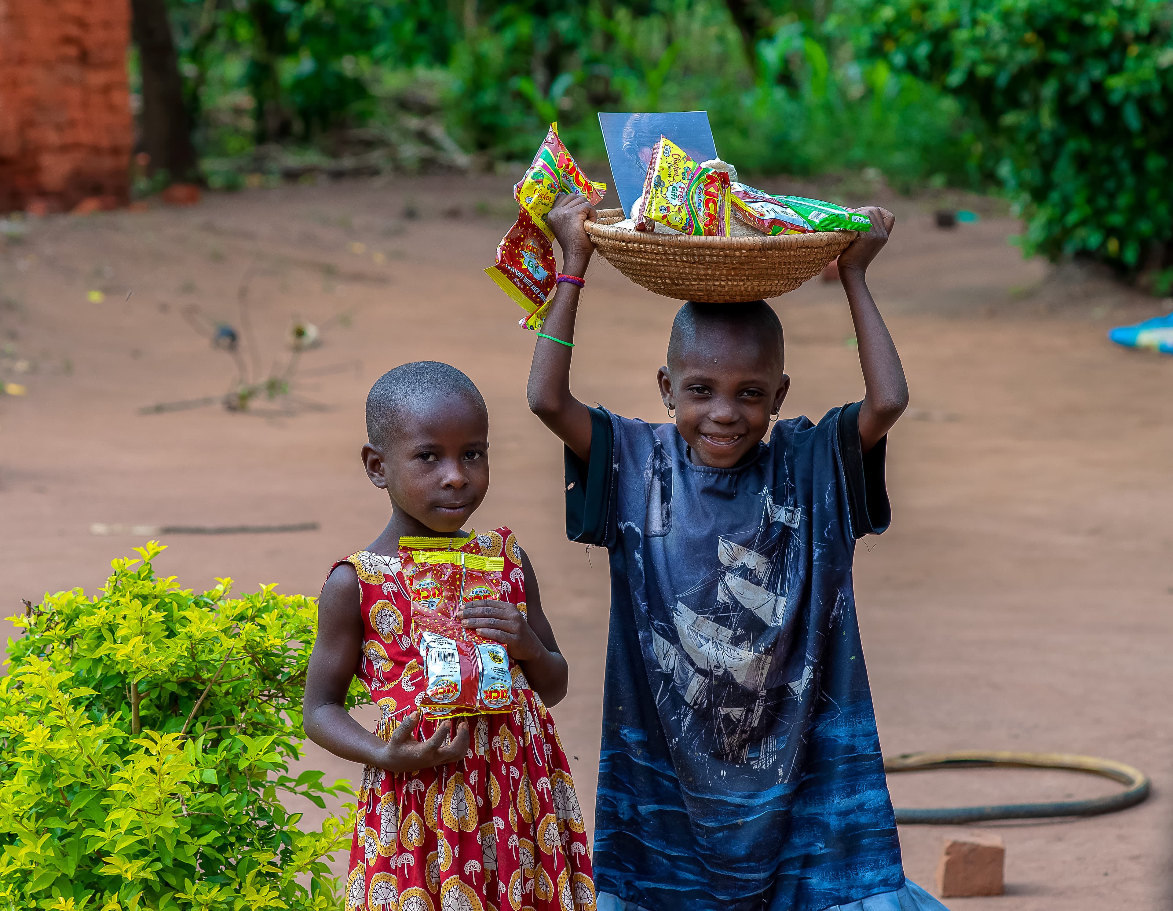 Two children carry food packages, one balancing a bowl of goods on her head.