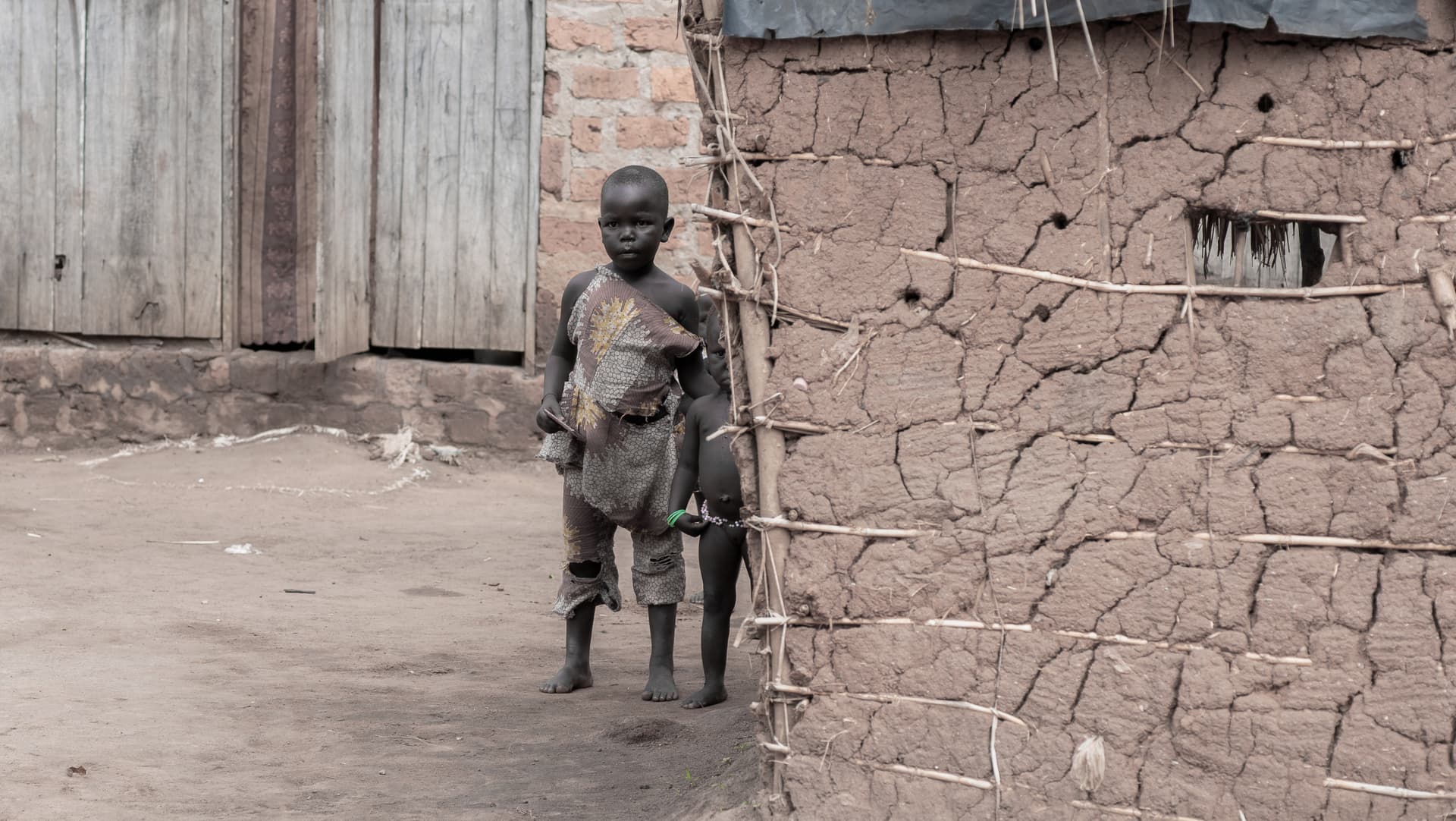 A young child stands alone beside a mud brick wall.