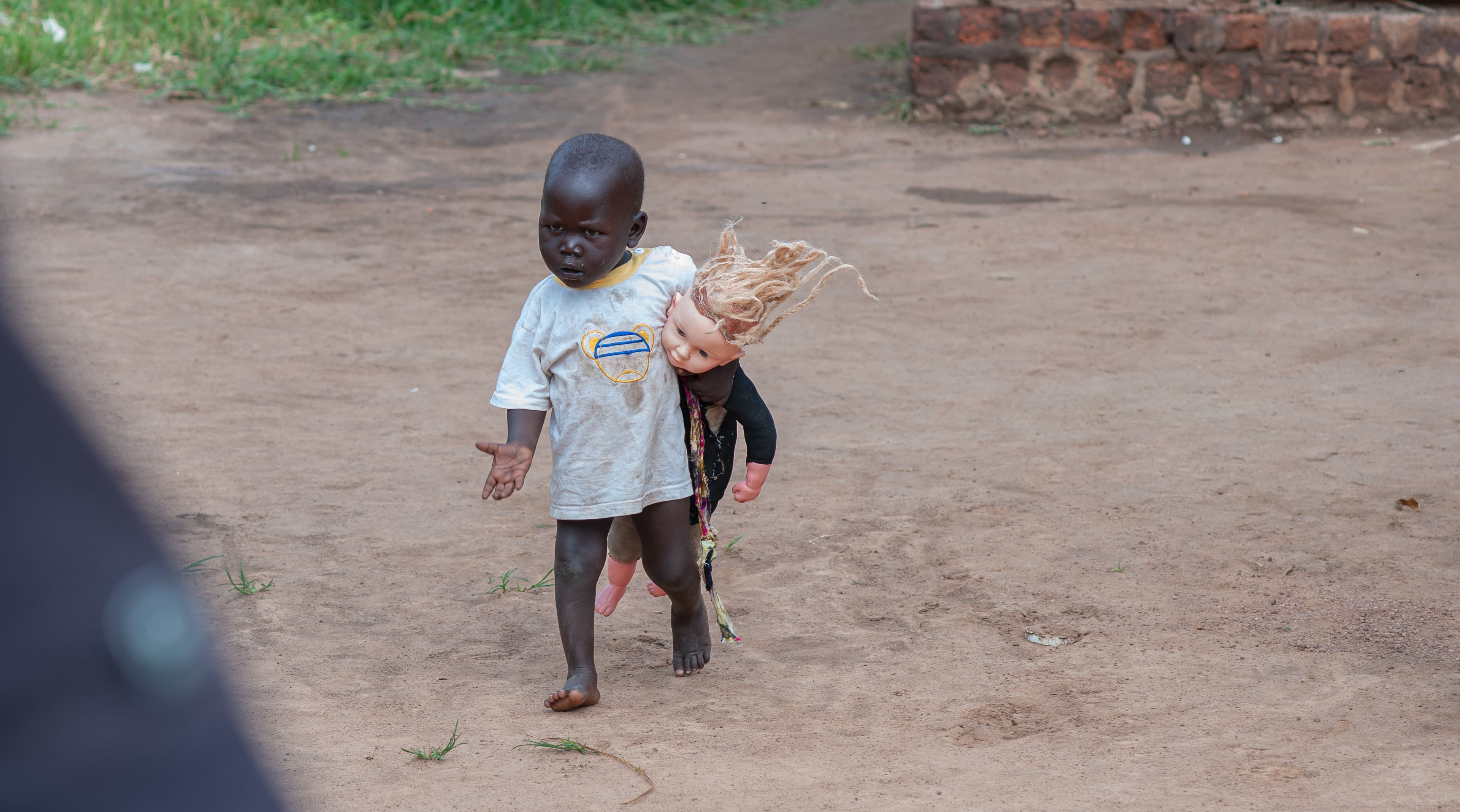 A child walks along a dirt path carrying a small bundle.