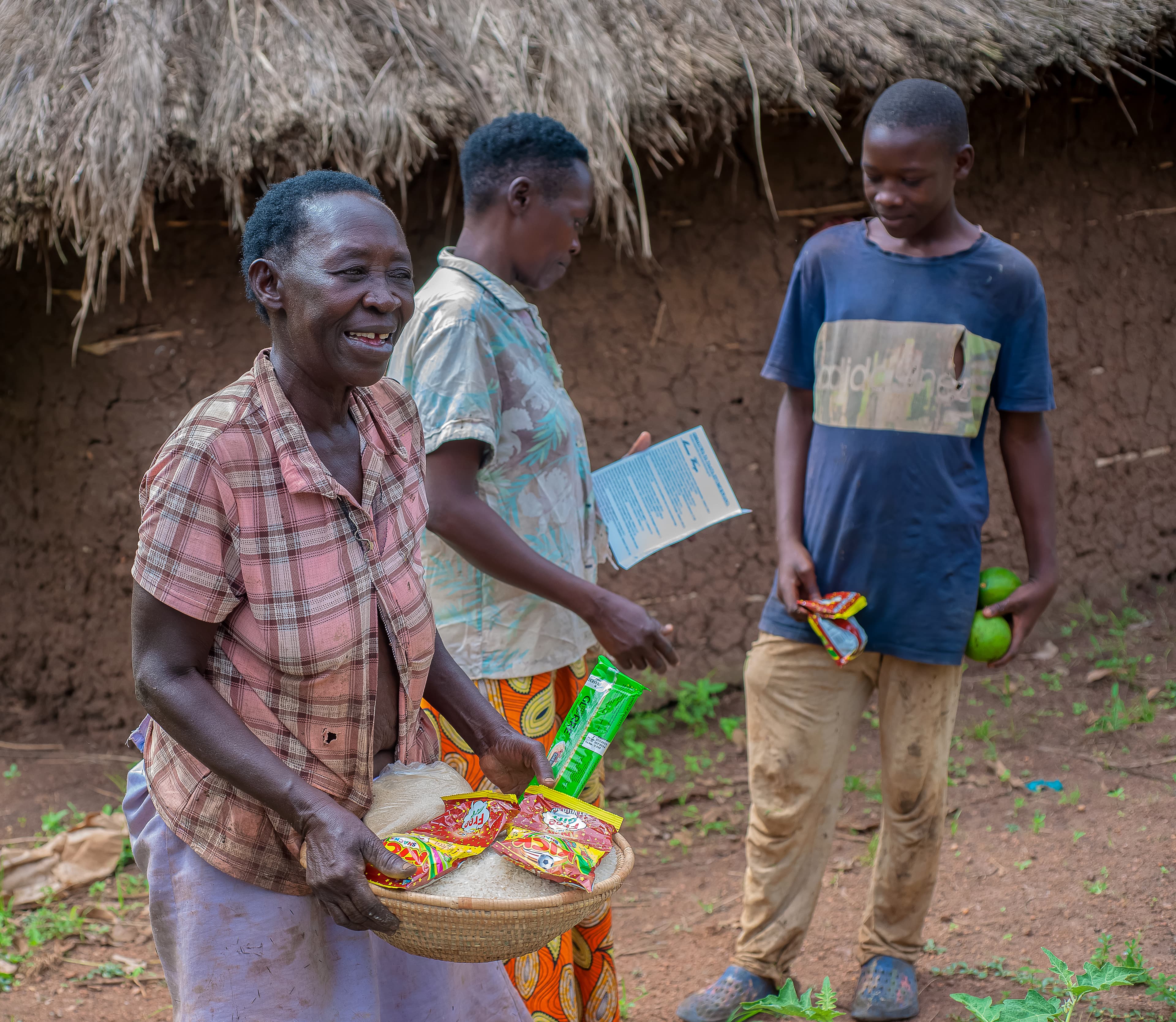An elderly woman smiles while receiving a food package from two JFM volunteers.