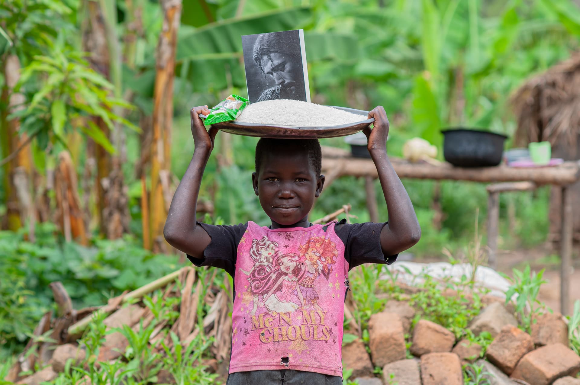 A girl in a pink top holds a plate with a photo above her head in a garden.