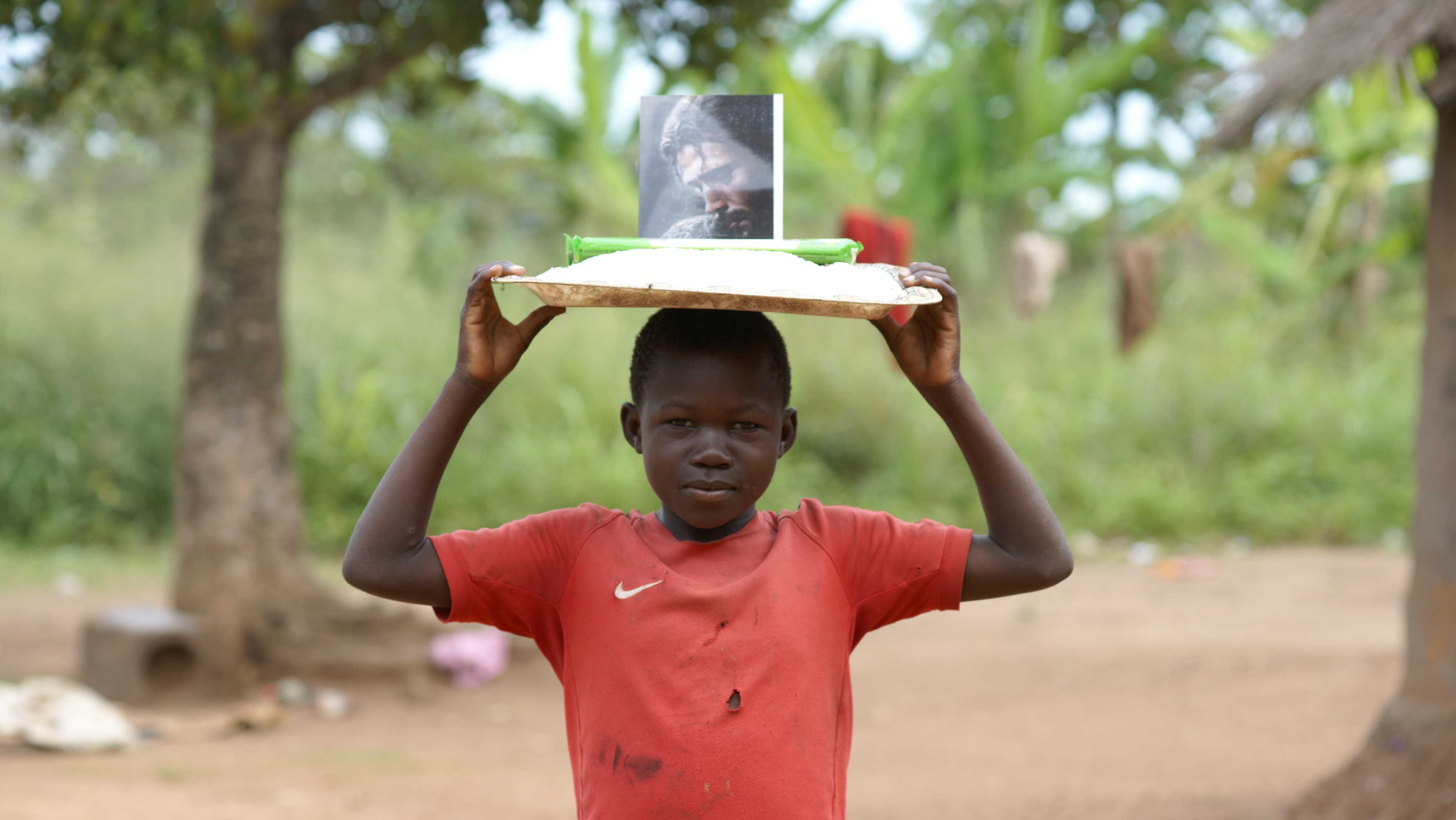 A boy in a red shirt holds a plate with a printed photo above his head.