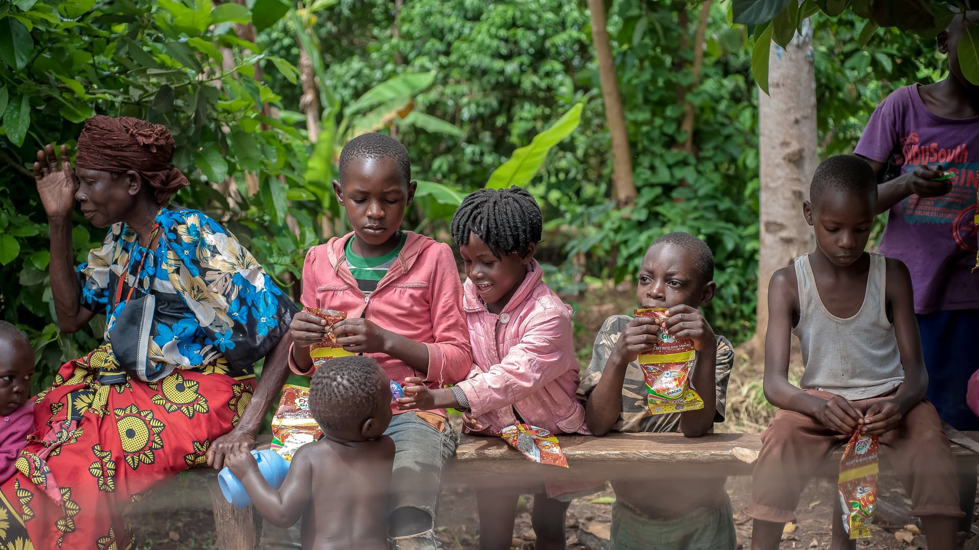 A woman and several children sit together outdoors as a family group.