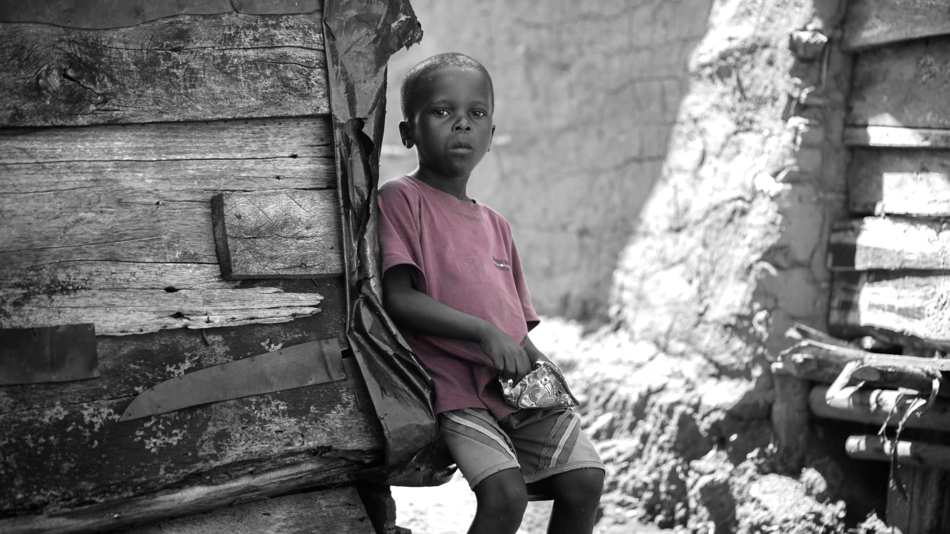 Black-and-white photo of a child sitting on a wooden structure outdoors.
