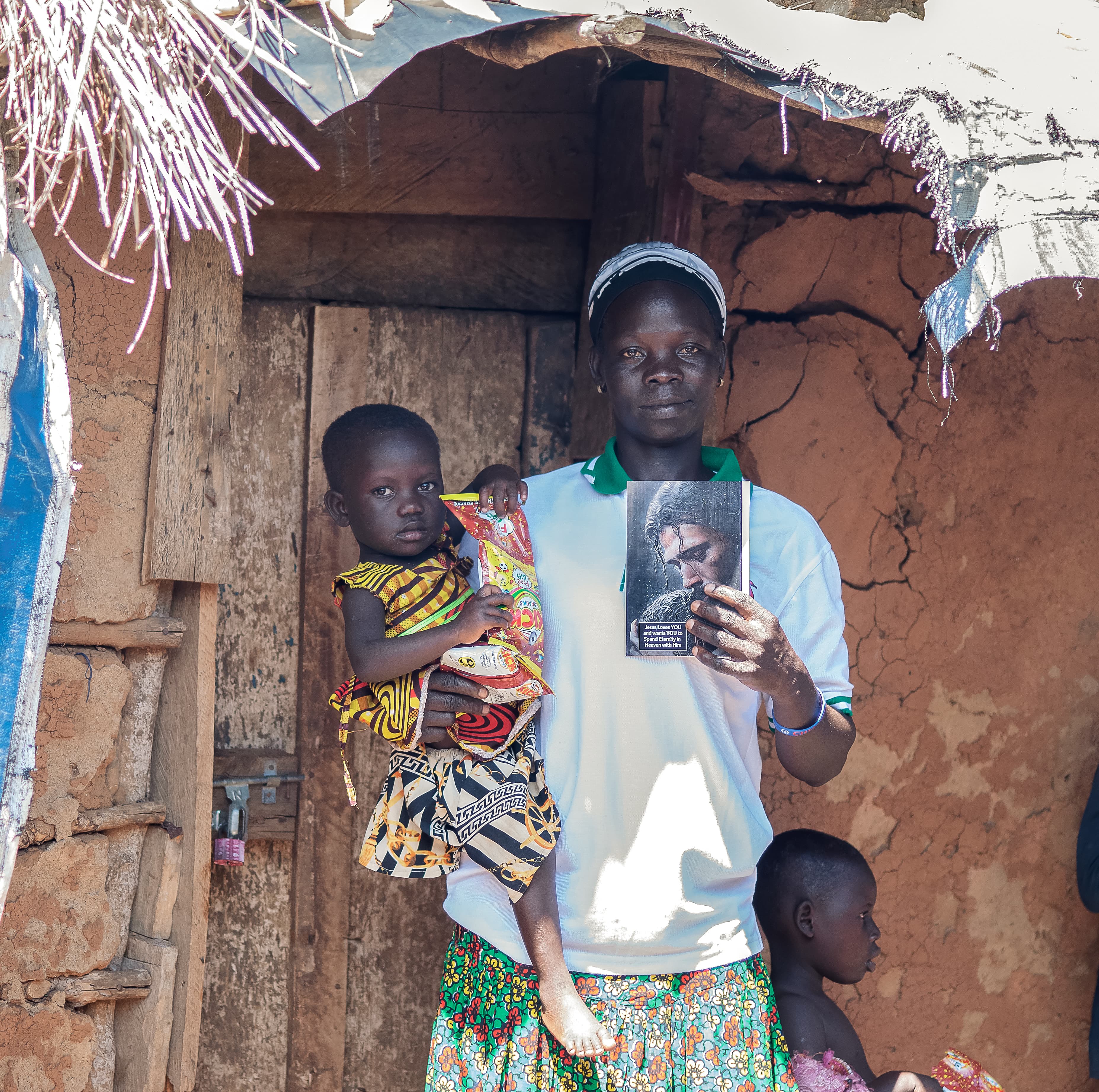 A woman stands with three children in a doorway, one child holding a printed photo.