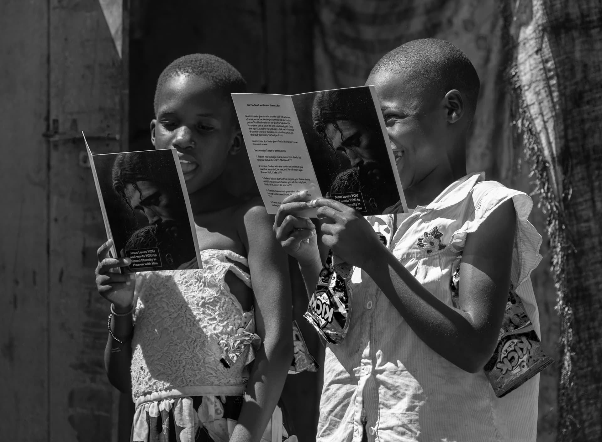 Black-and-white photo of two children reading a printed photo or booklet together.