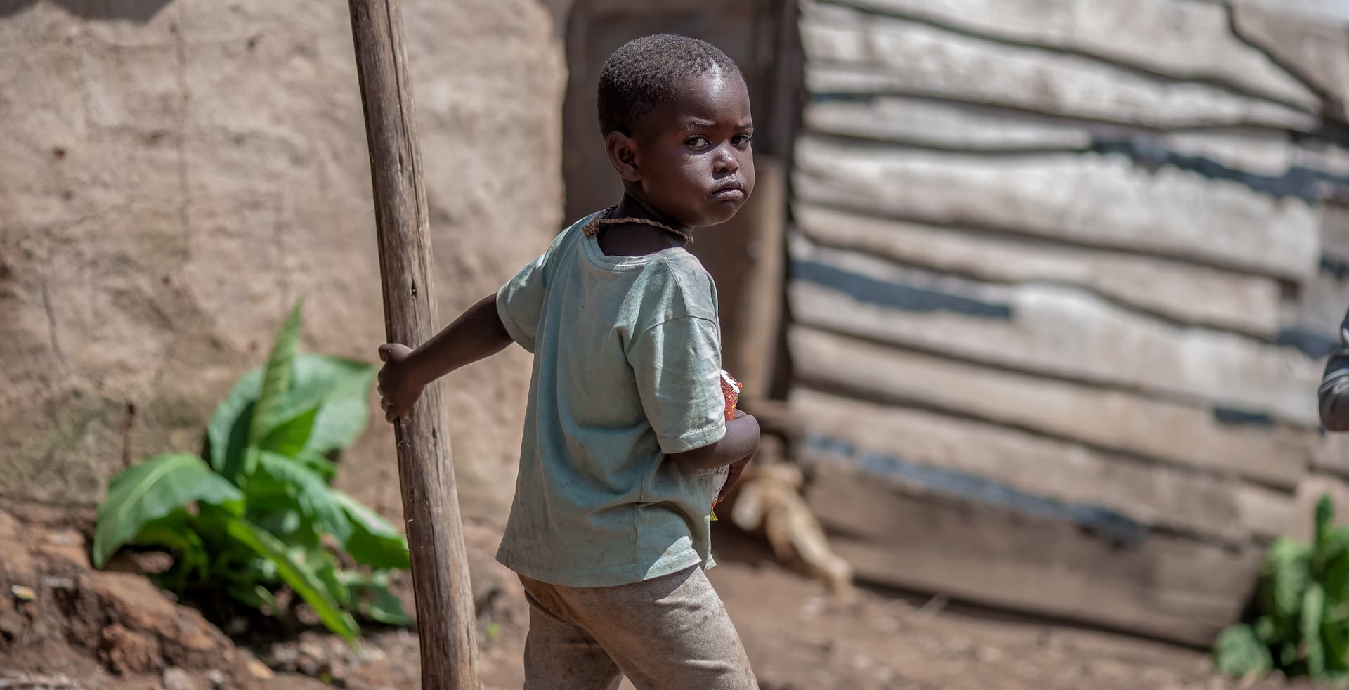 A child in a green shirt walks near a small wooden shed structure.