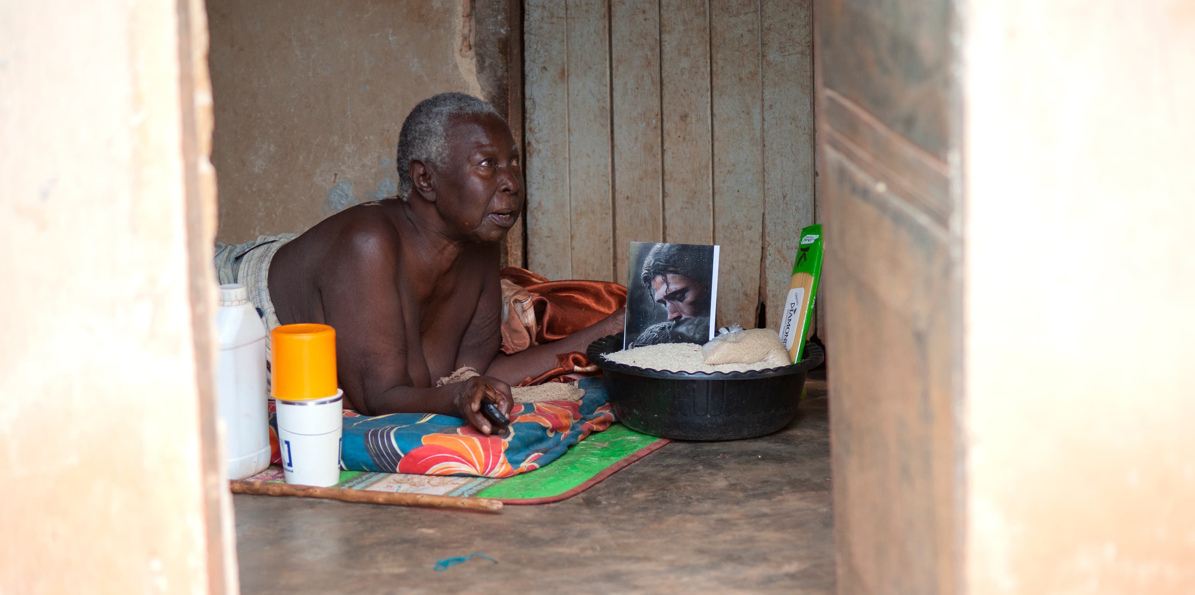 A shirtless man sits on the floor sorting food gift items in a doorway.