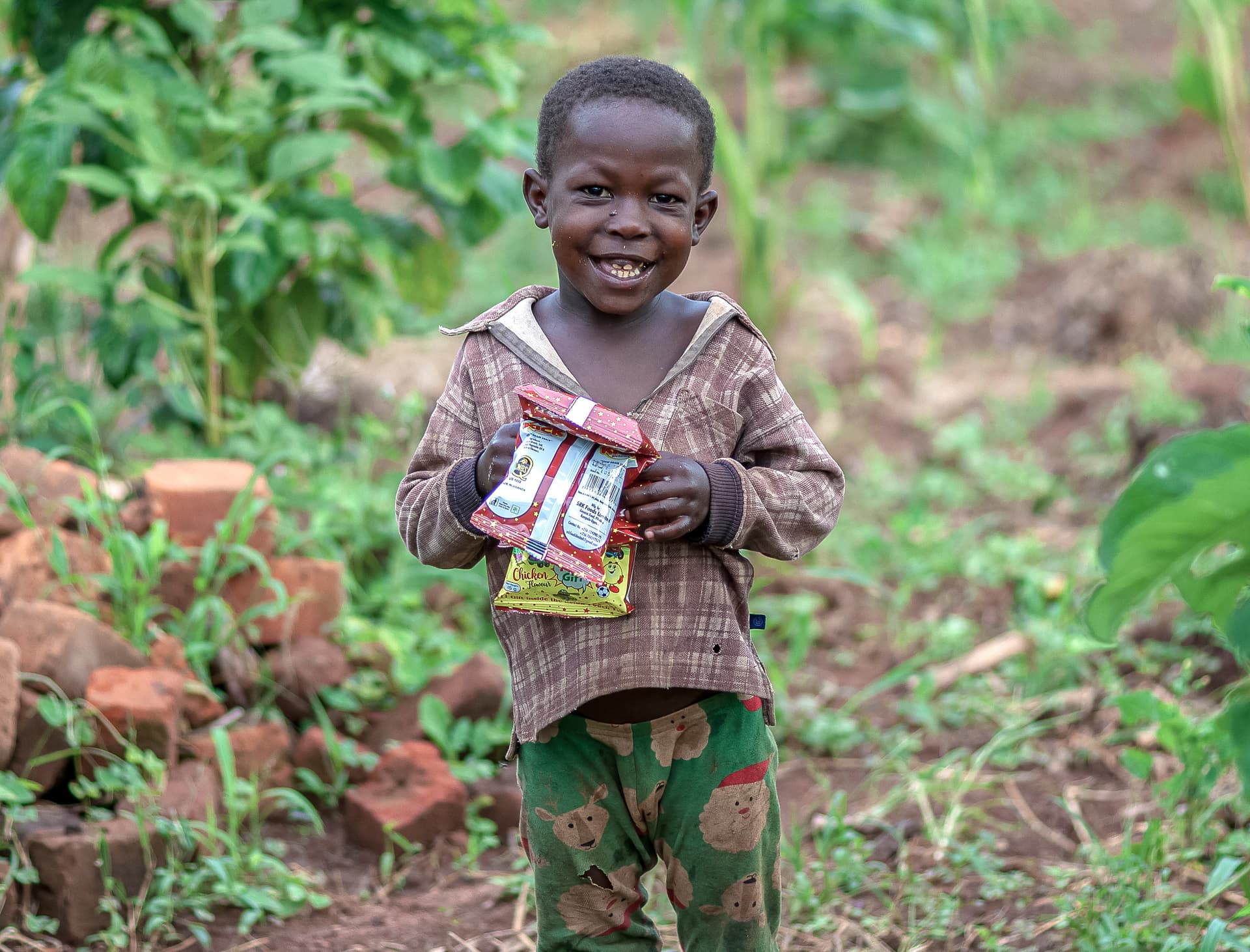 A small child stands outdoors holding a food gift bag.