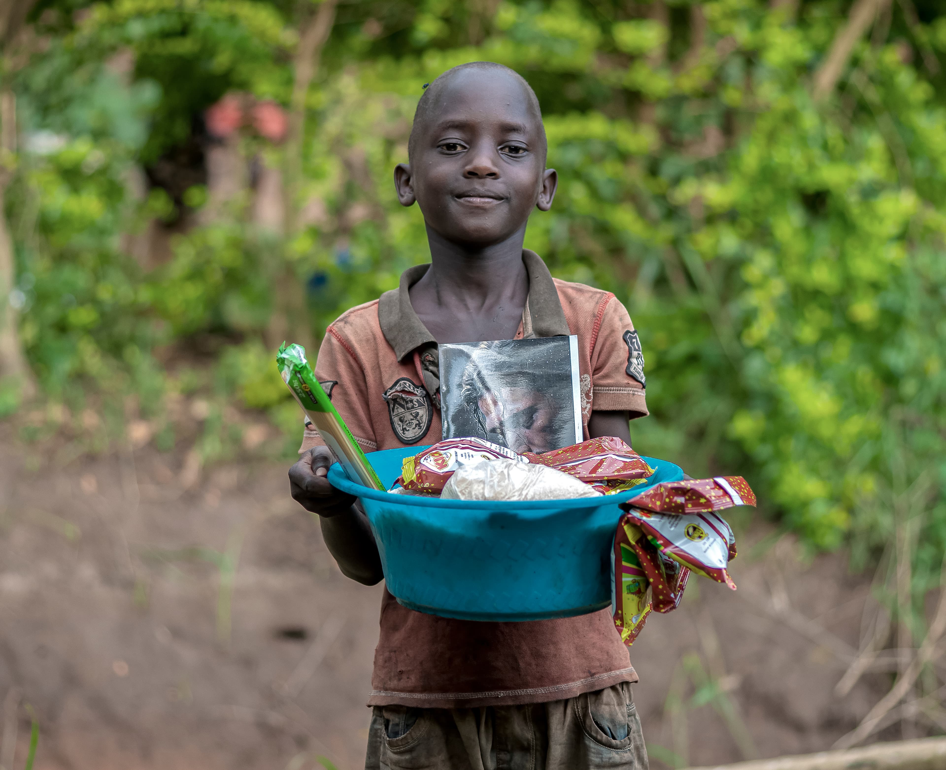 A child holds a blue basin containing food items and a printed photo.