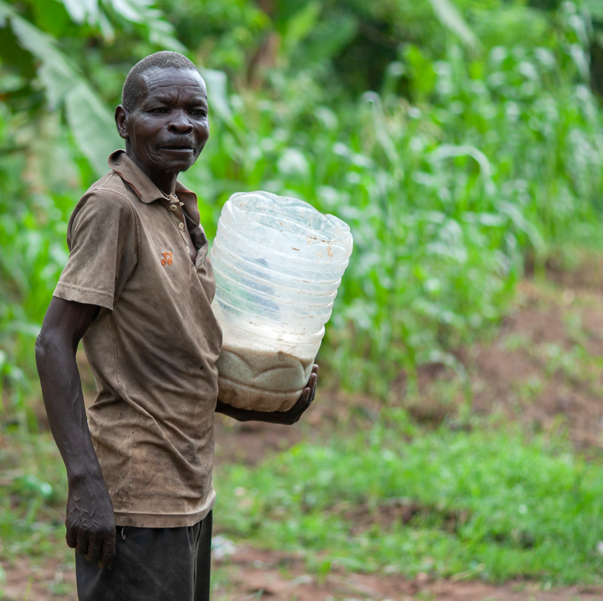 A man in a village setting carries a white plastic jerrycan of water or supplies.