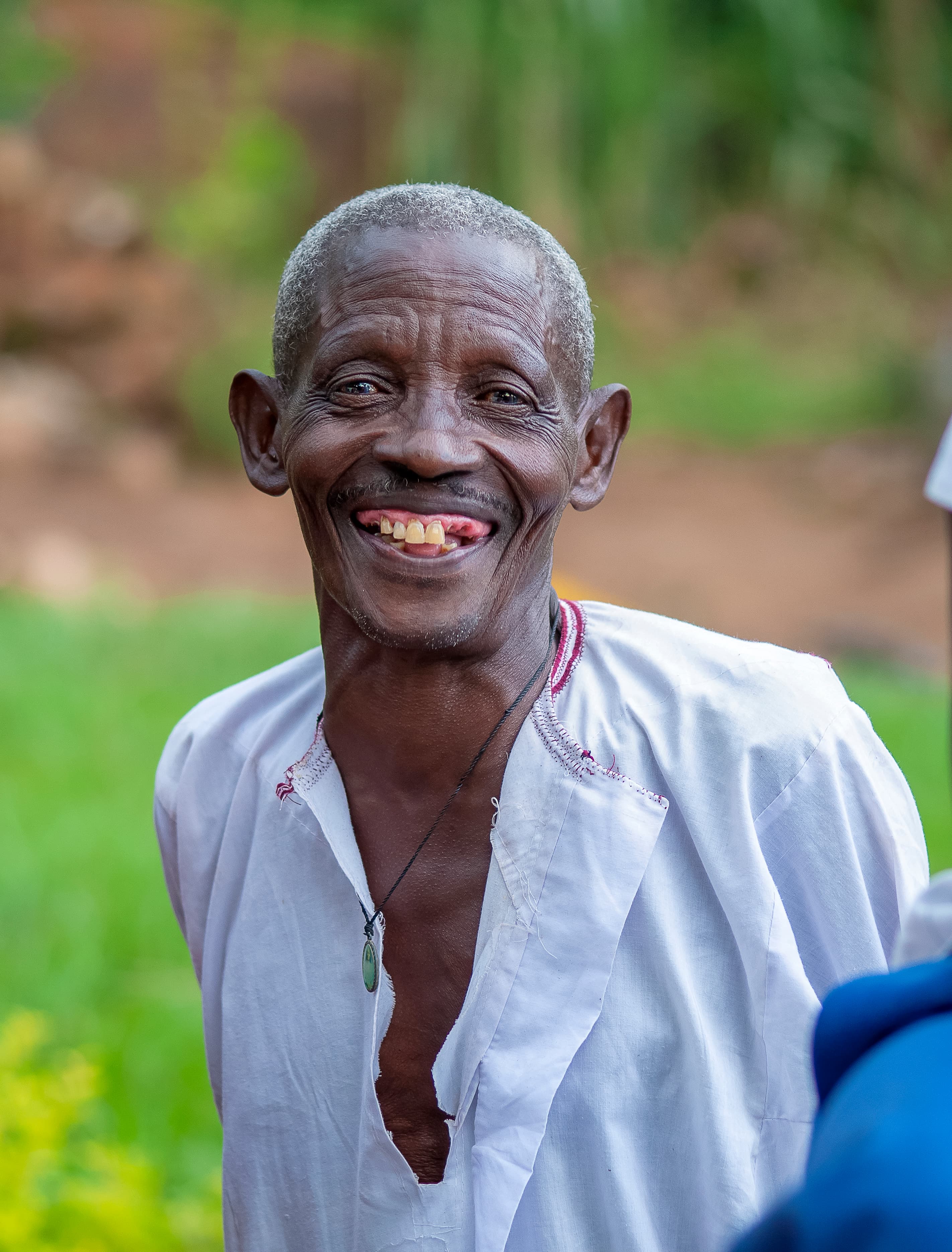 An elderly man in a white shirt smiles for the camera outdoors.