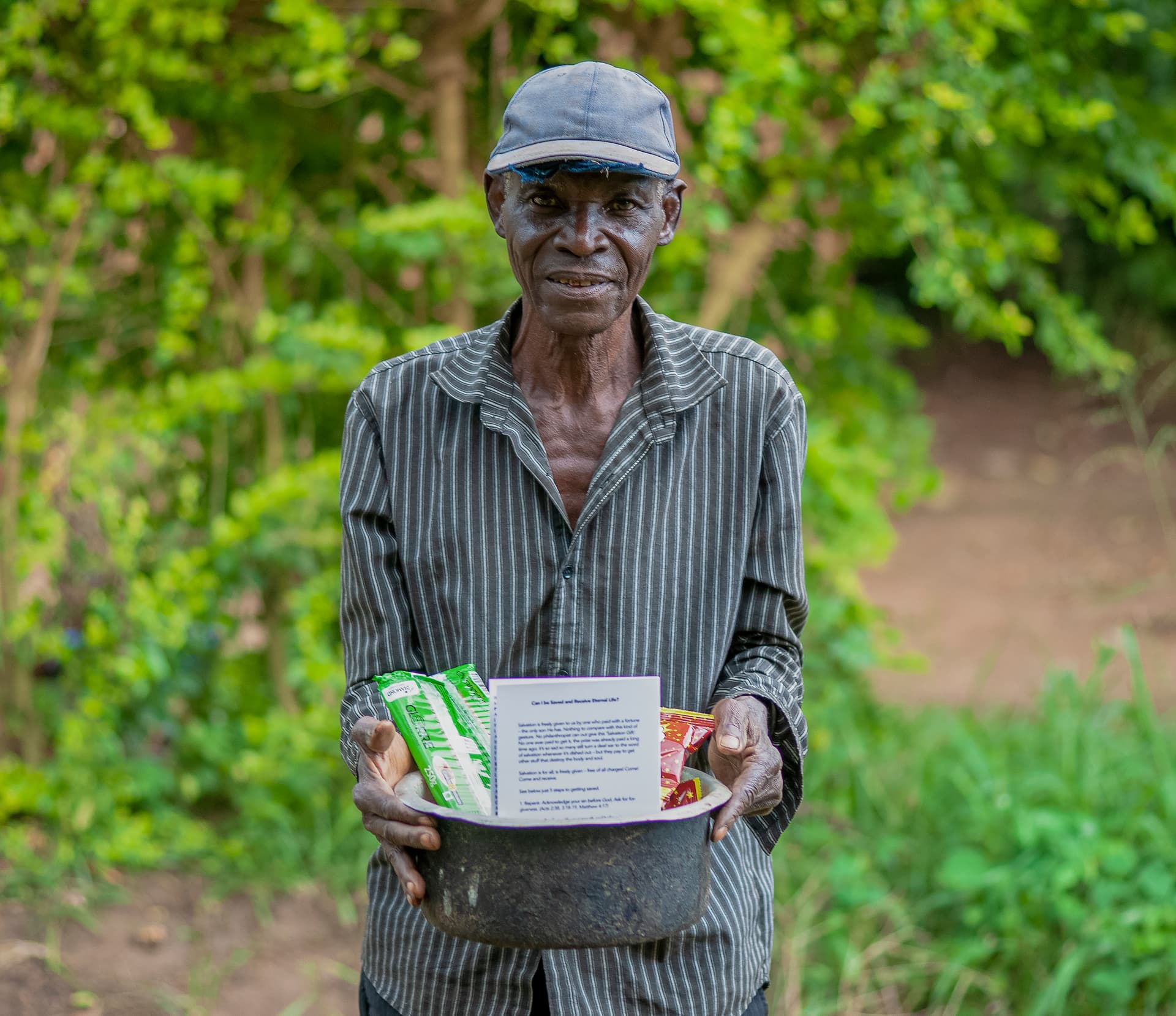 An elderly man wearing a cap holds food items and a printed paper.