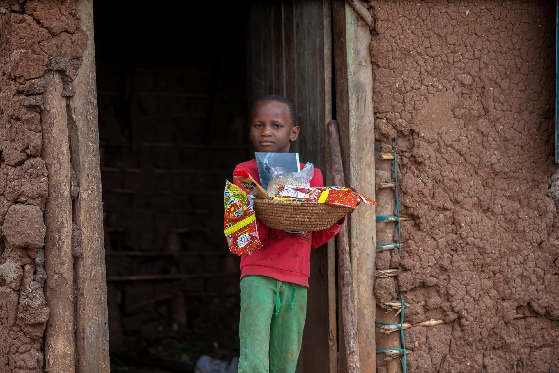 A child stands in a doorway holding a basket of food gift items.
