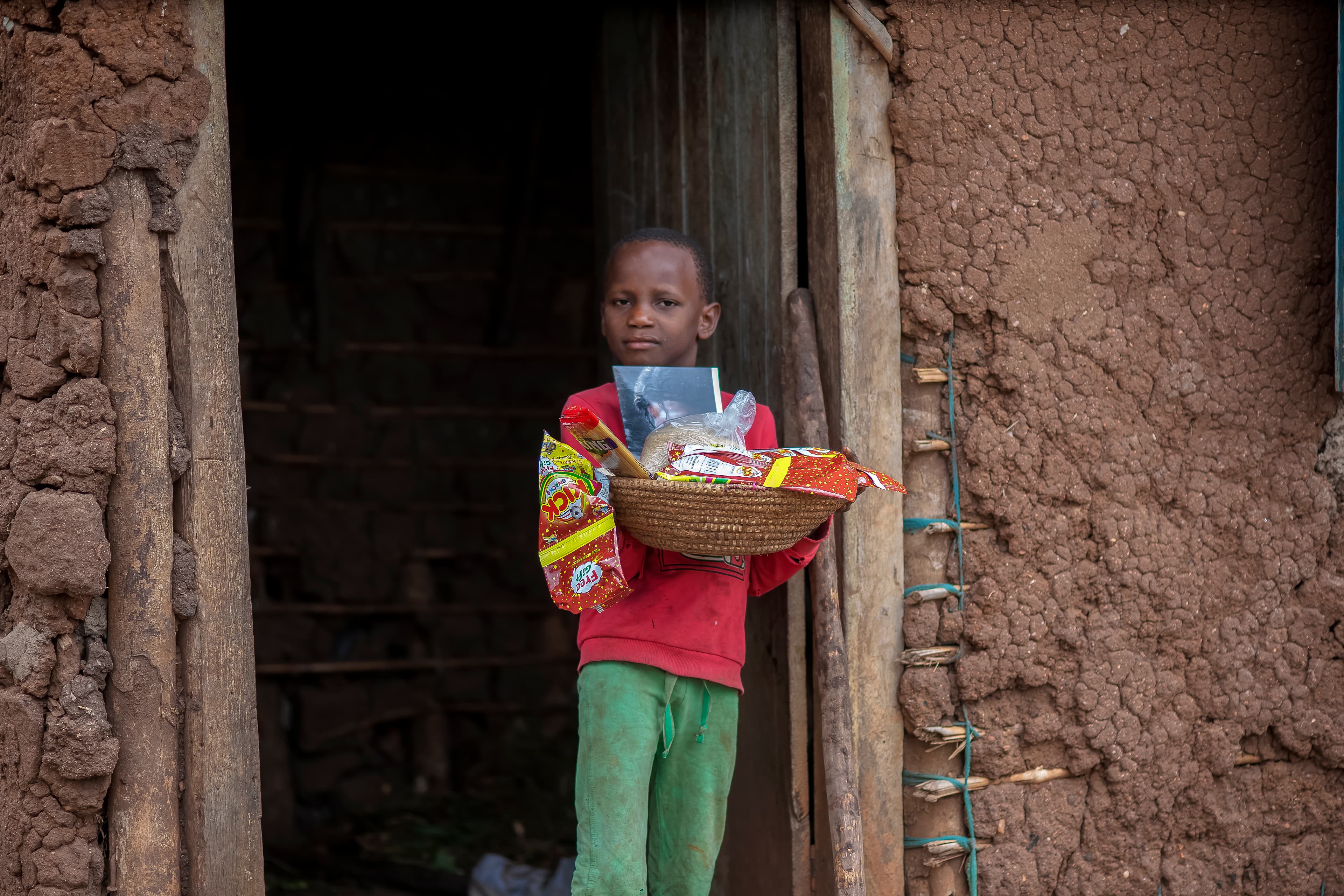 A child stands in a doorway holding a basket of food gift items.