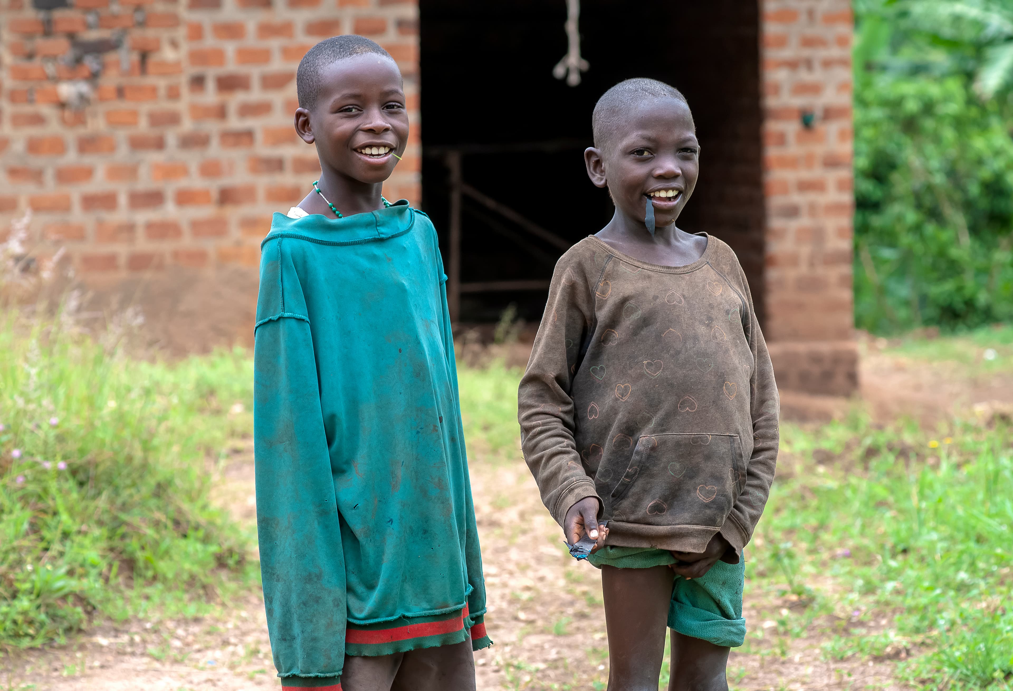 Two boys stand smiling side by side outside a brick building.