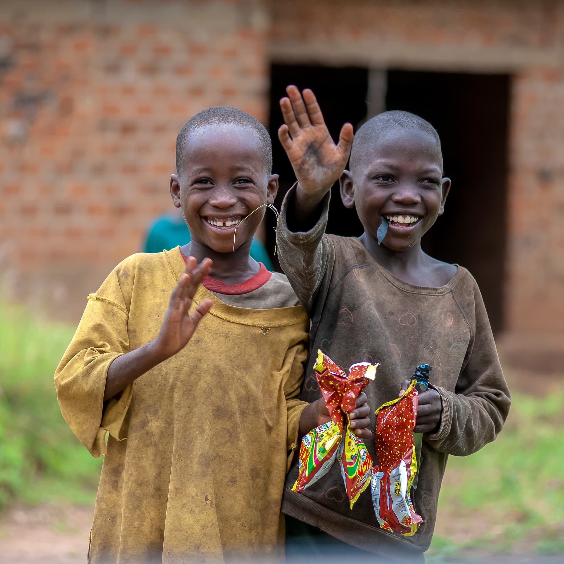 Two boys smile and wave, one holding a colorful food gift package.