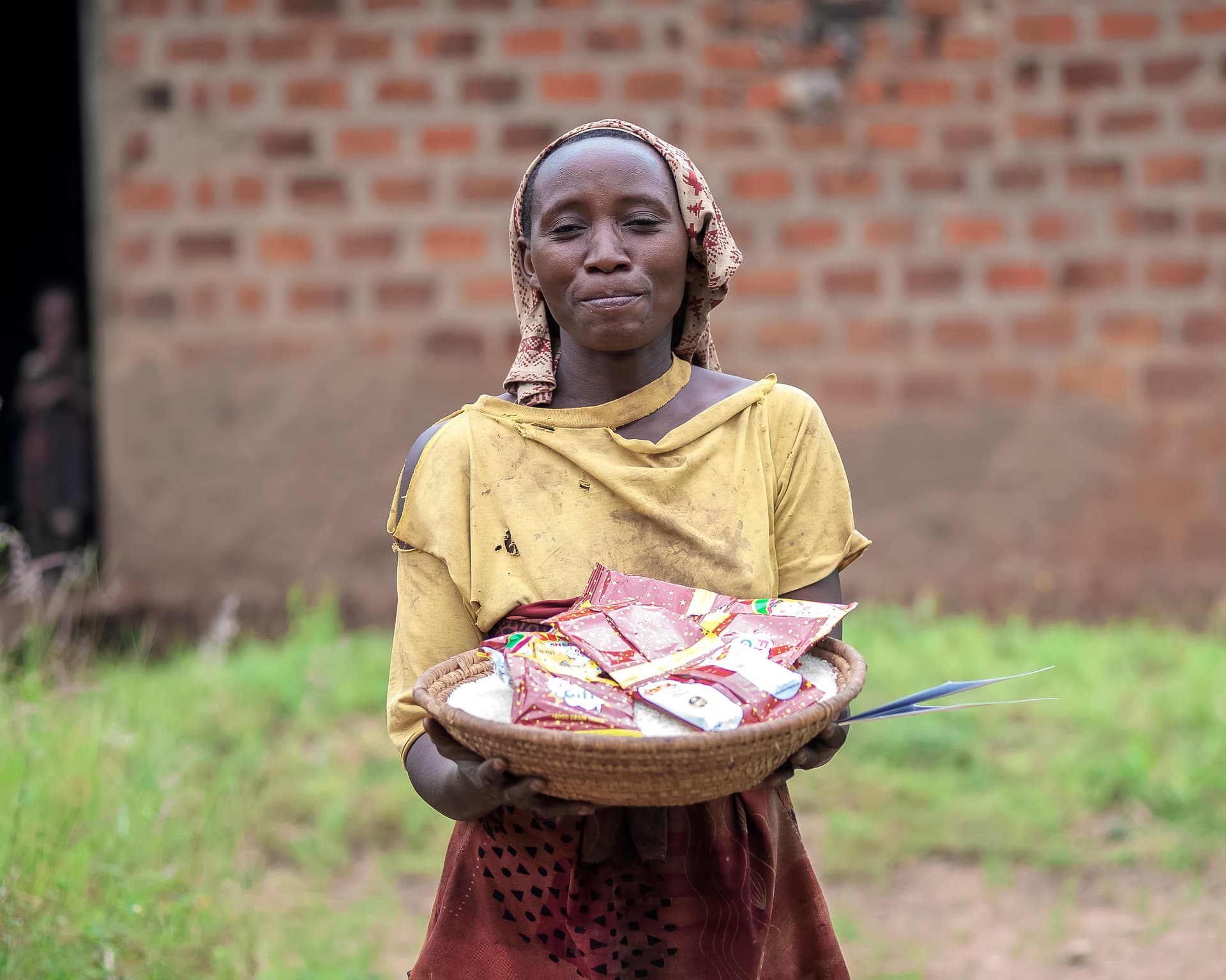 A girl in a yellow top holds a plate of food gifts outside a brick house.
