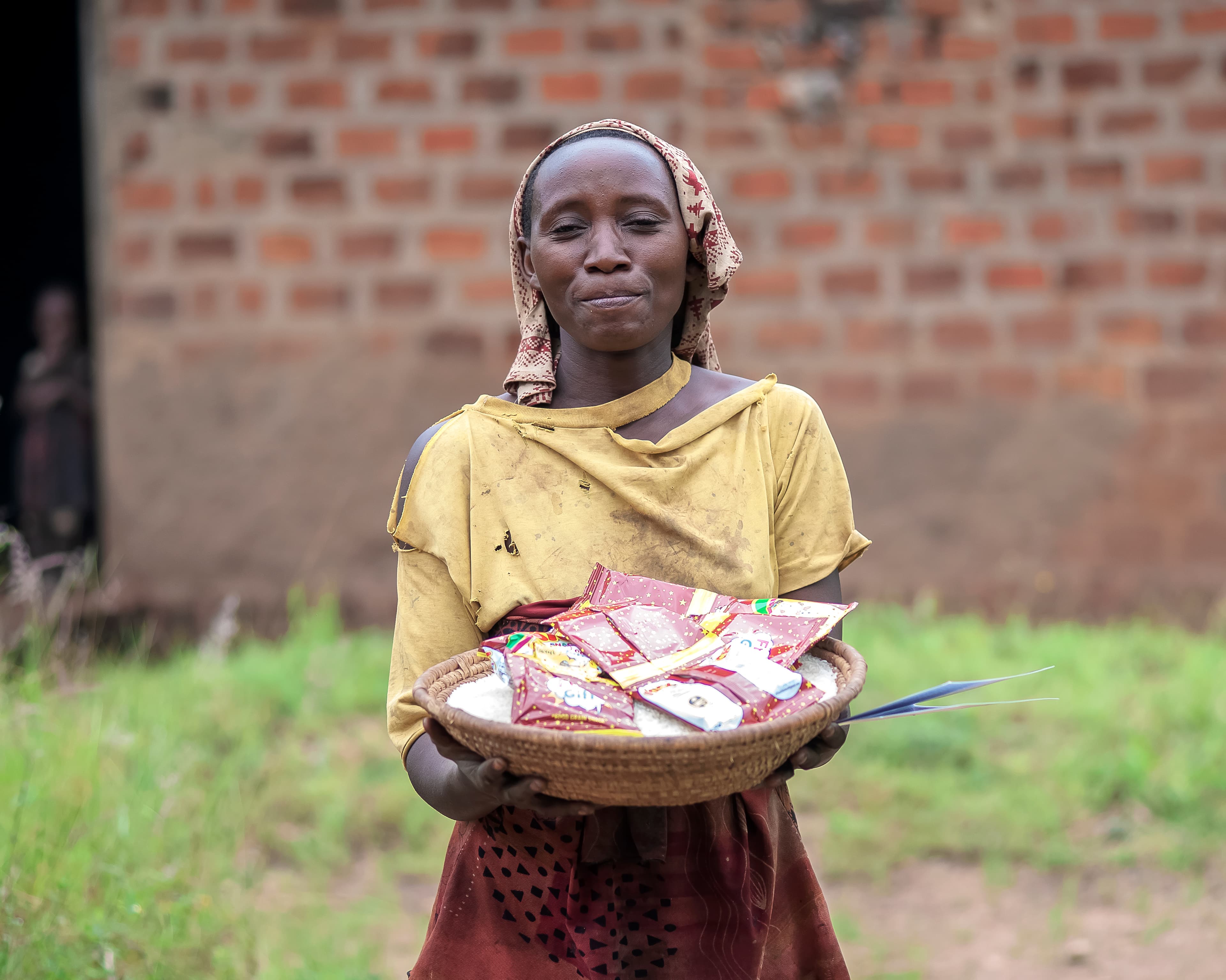 A girl in a yellow top holds a plate of food gifts outside a brick house.