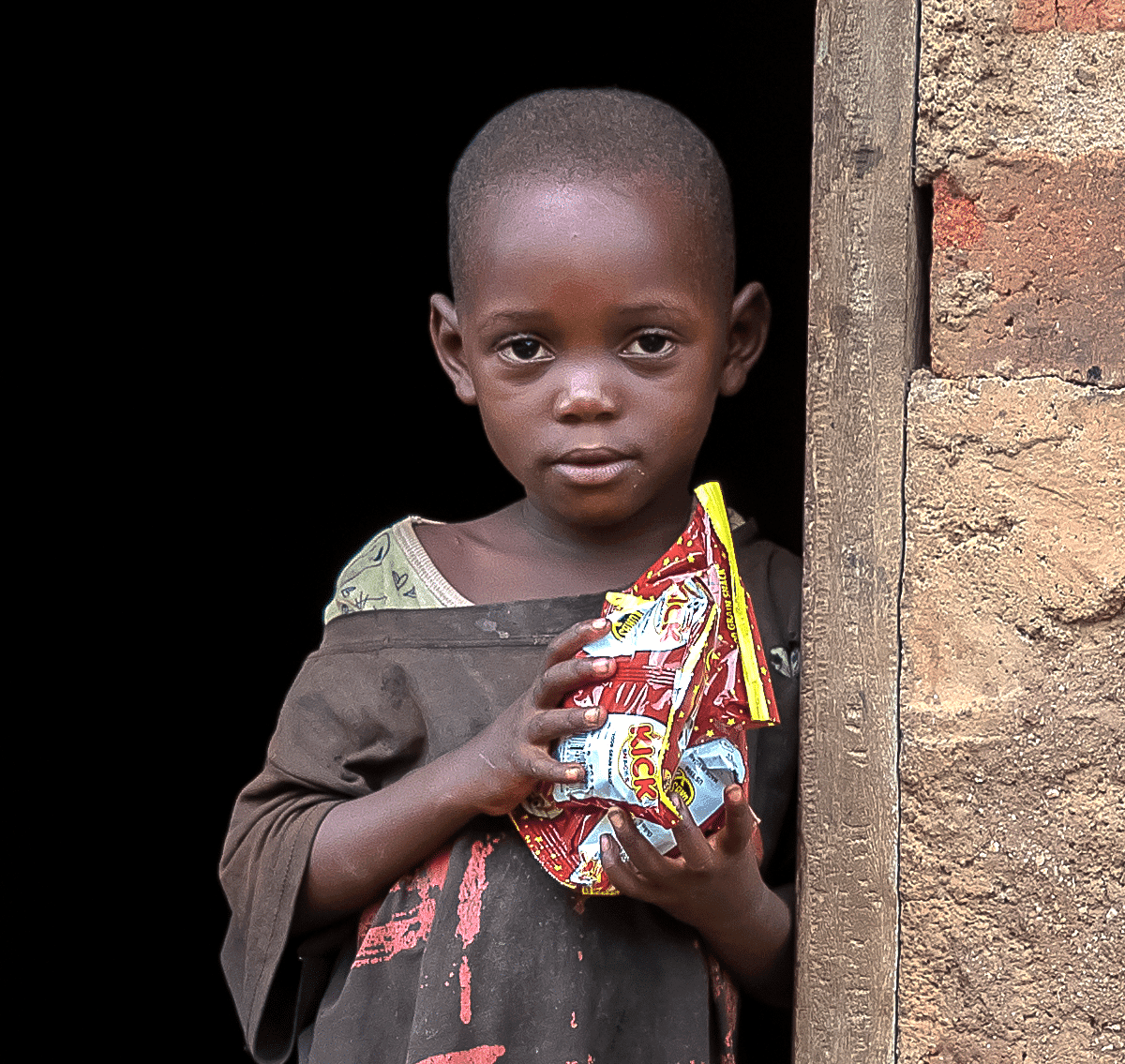 A young boy stands in a doorway holding a bag of snack food he received.