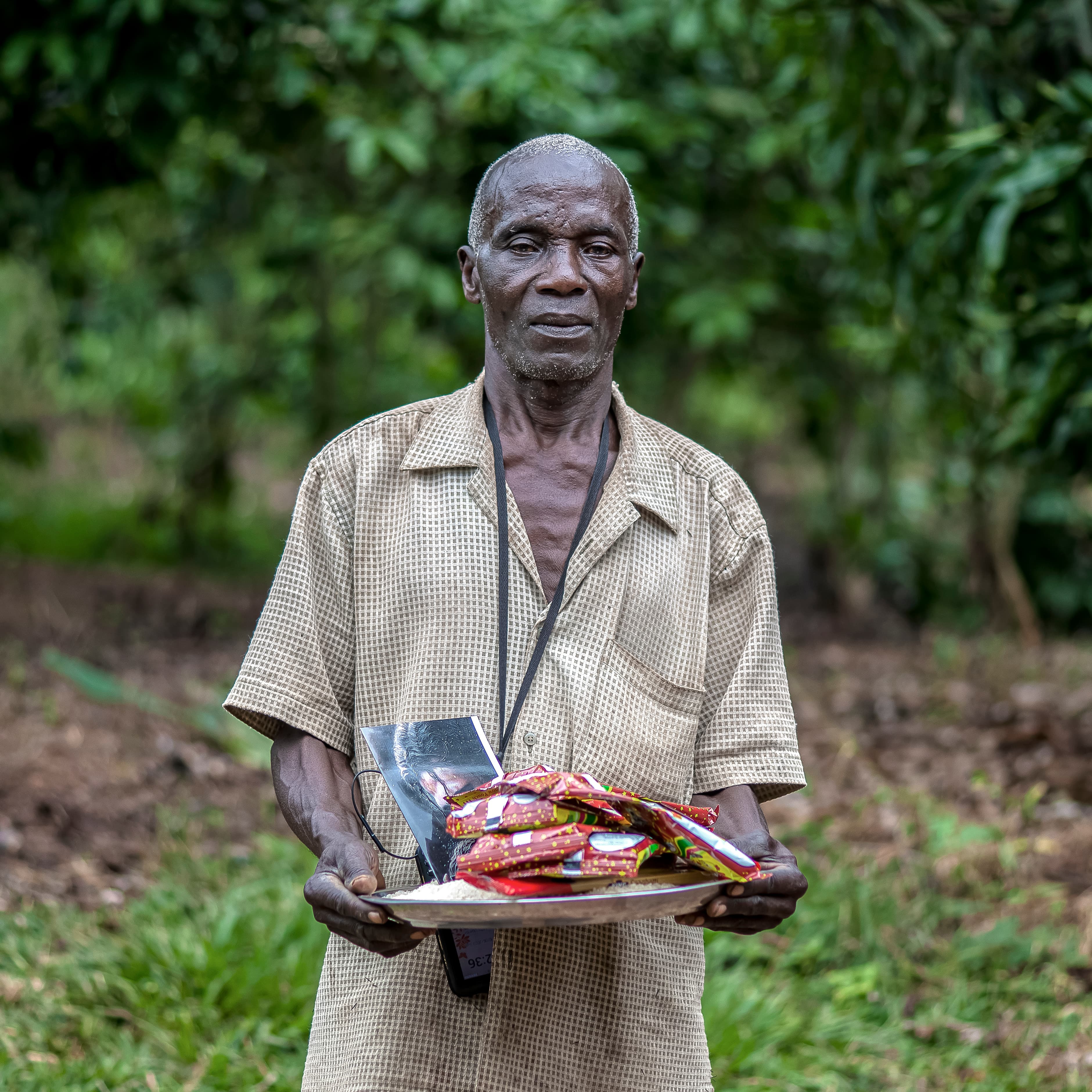An elderly man holds a plate stacked with food gift items outdoors.
