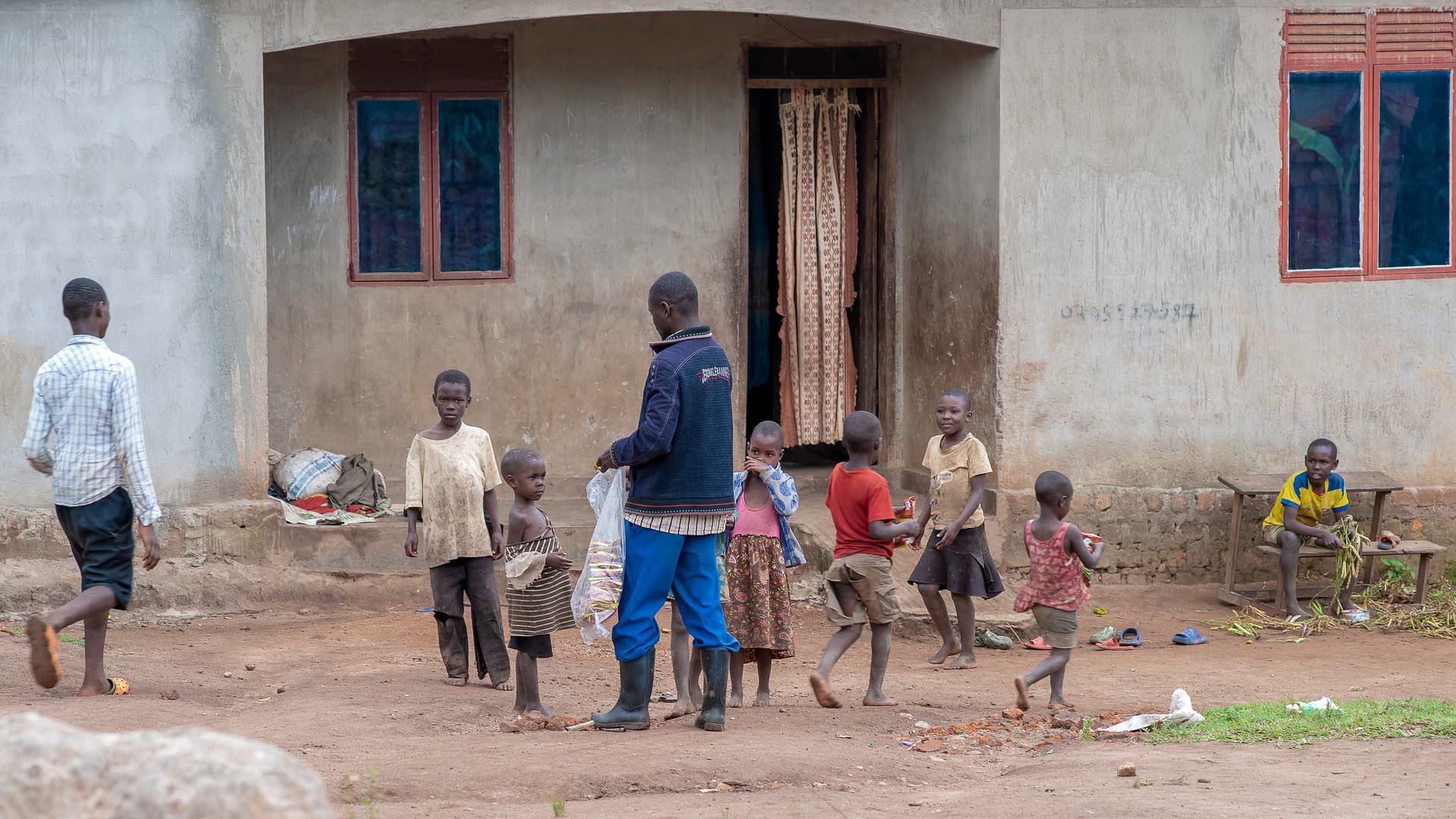 A group of children play and gather outside a brick building in the village.