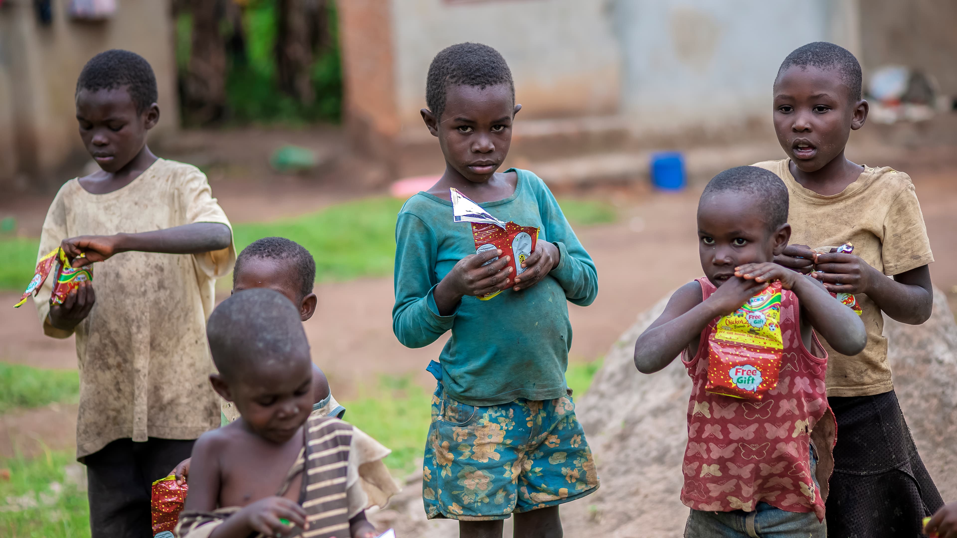 A group of children stand together outdoors, one holding a small food item, near Teluma village.