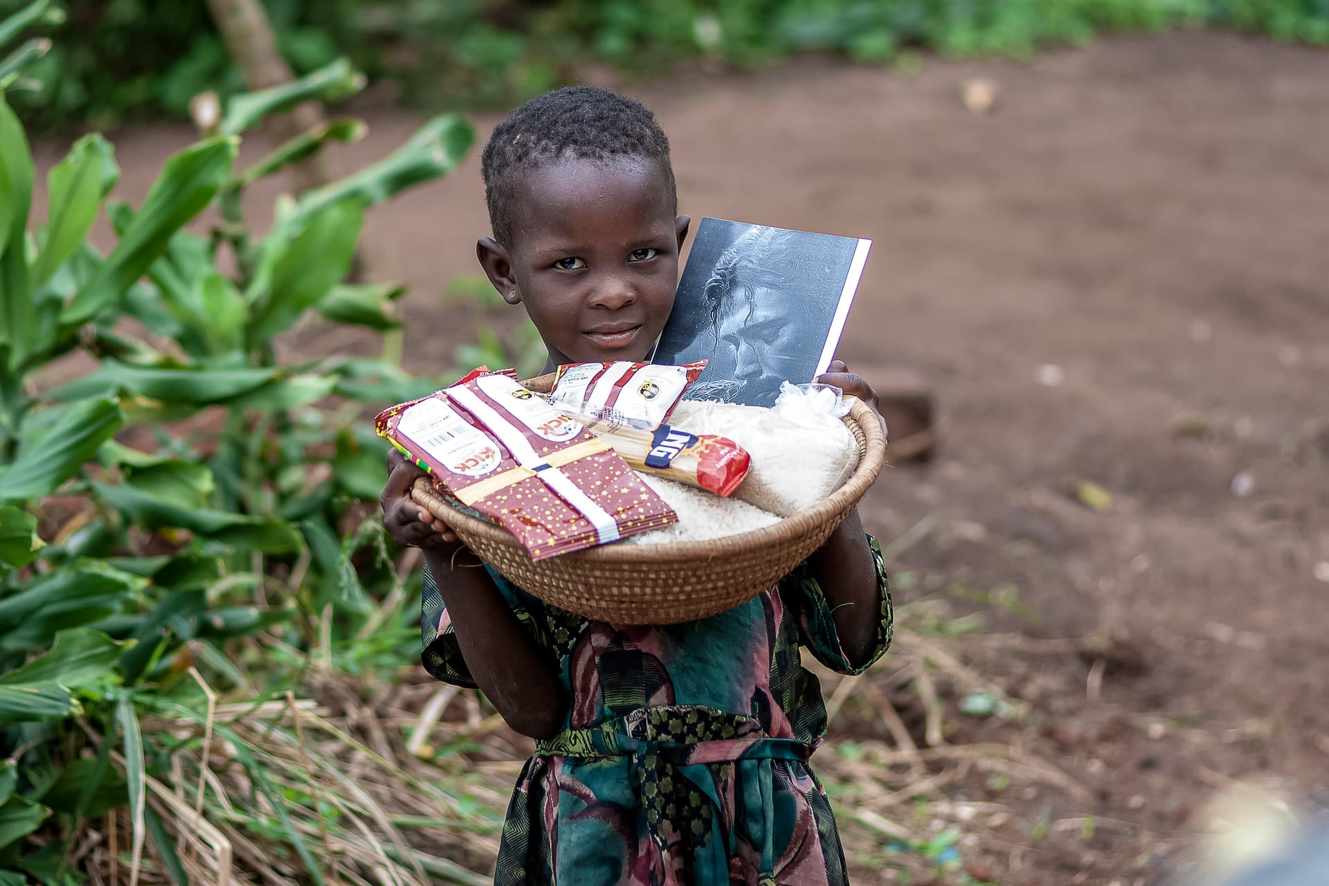 A child holds a plate of food gifts including a printed photo, standing outdoors.