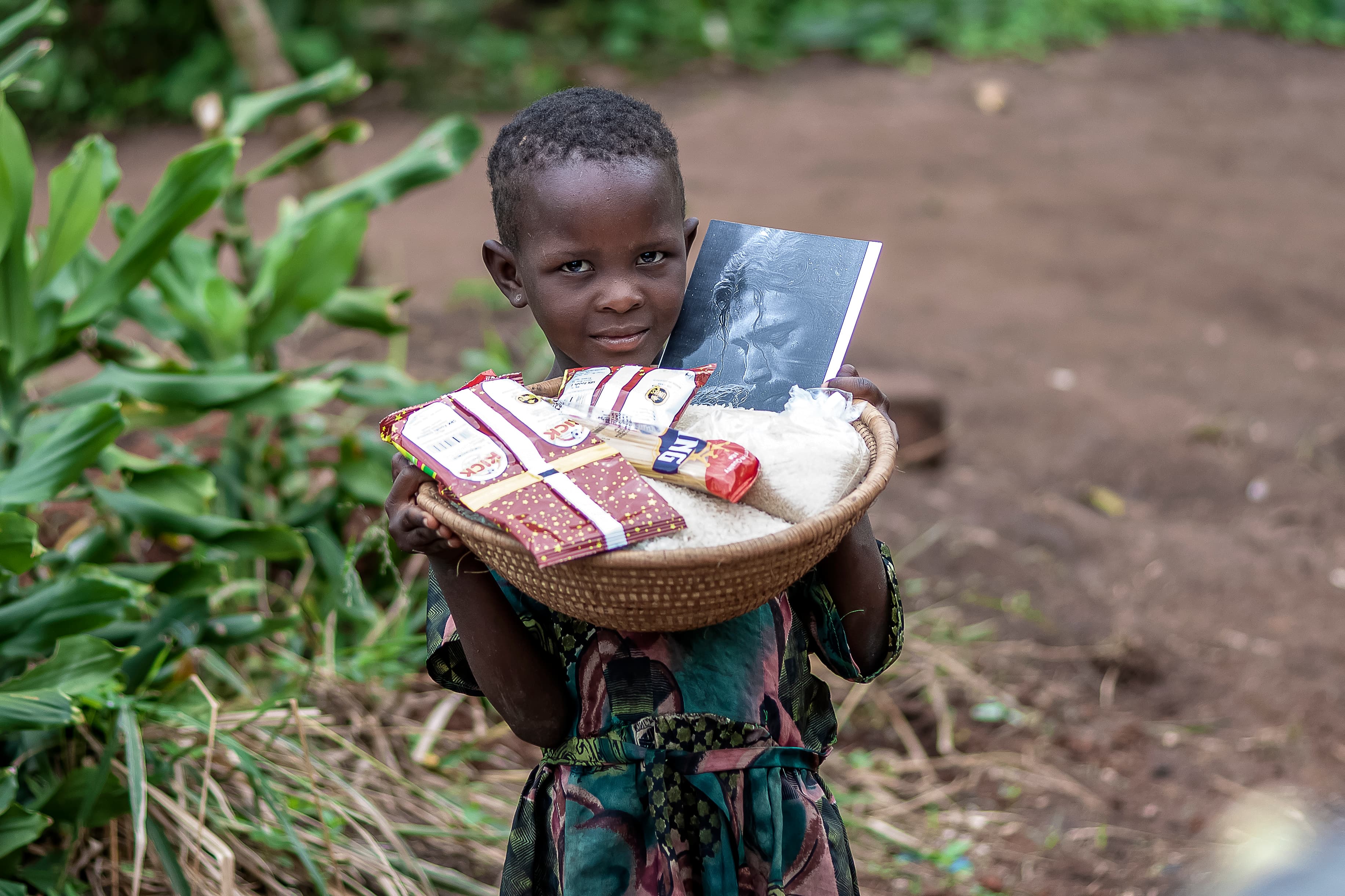 A child holds a plate of food gifts including a printed photo, standing outdoors.