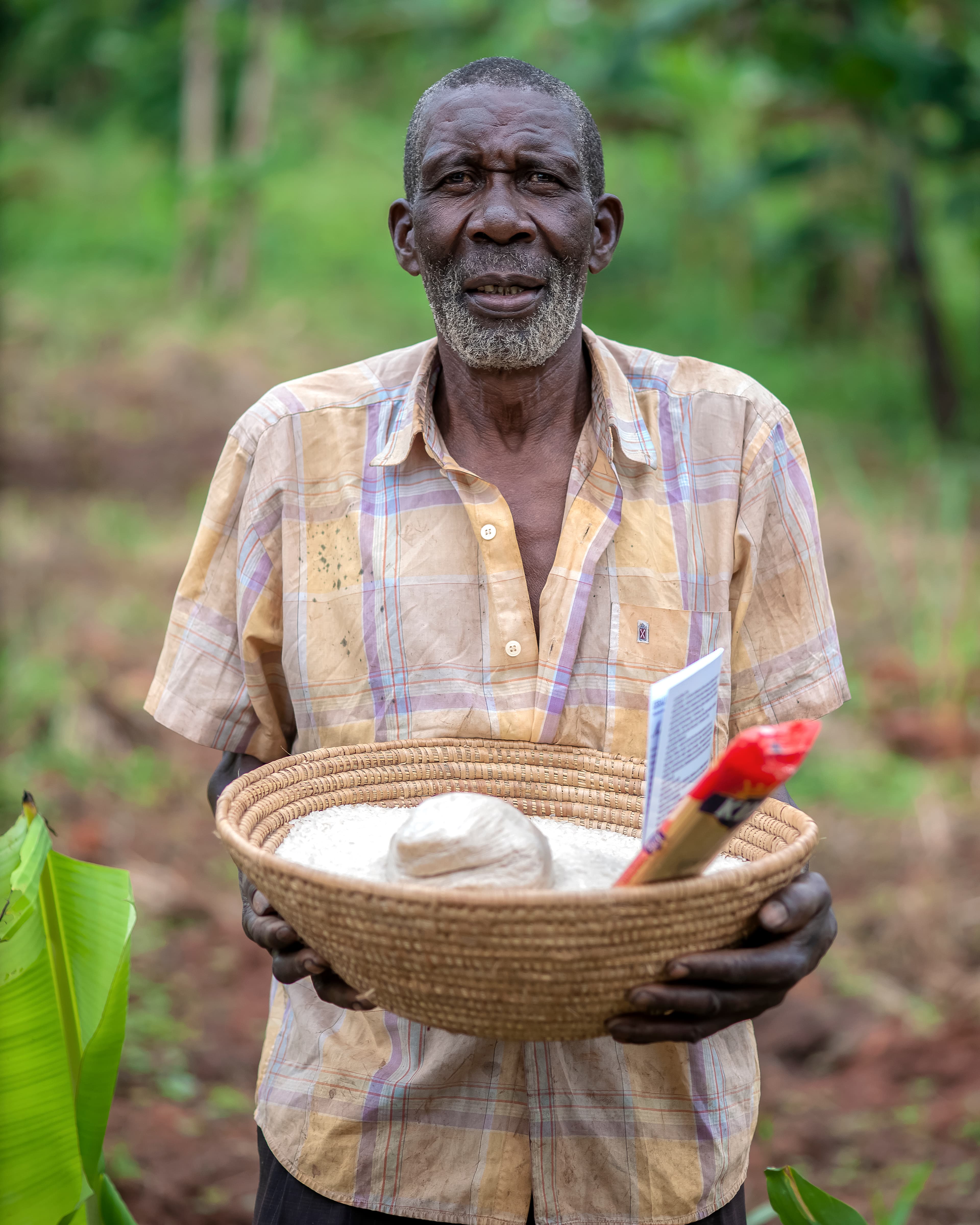 An elderly man holds a woven basket filled with food items and a small photo.