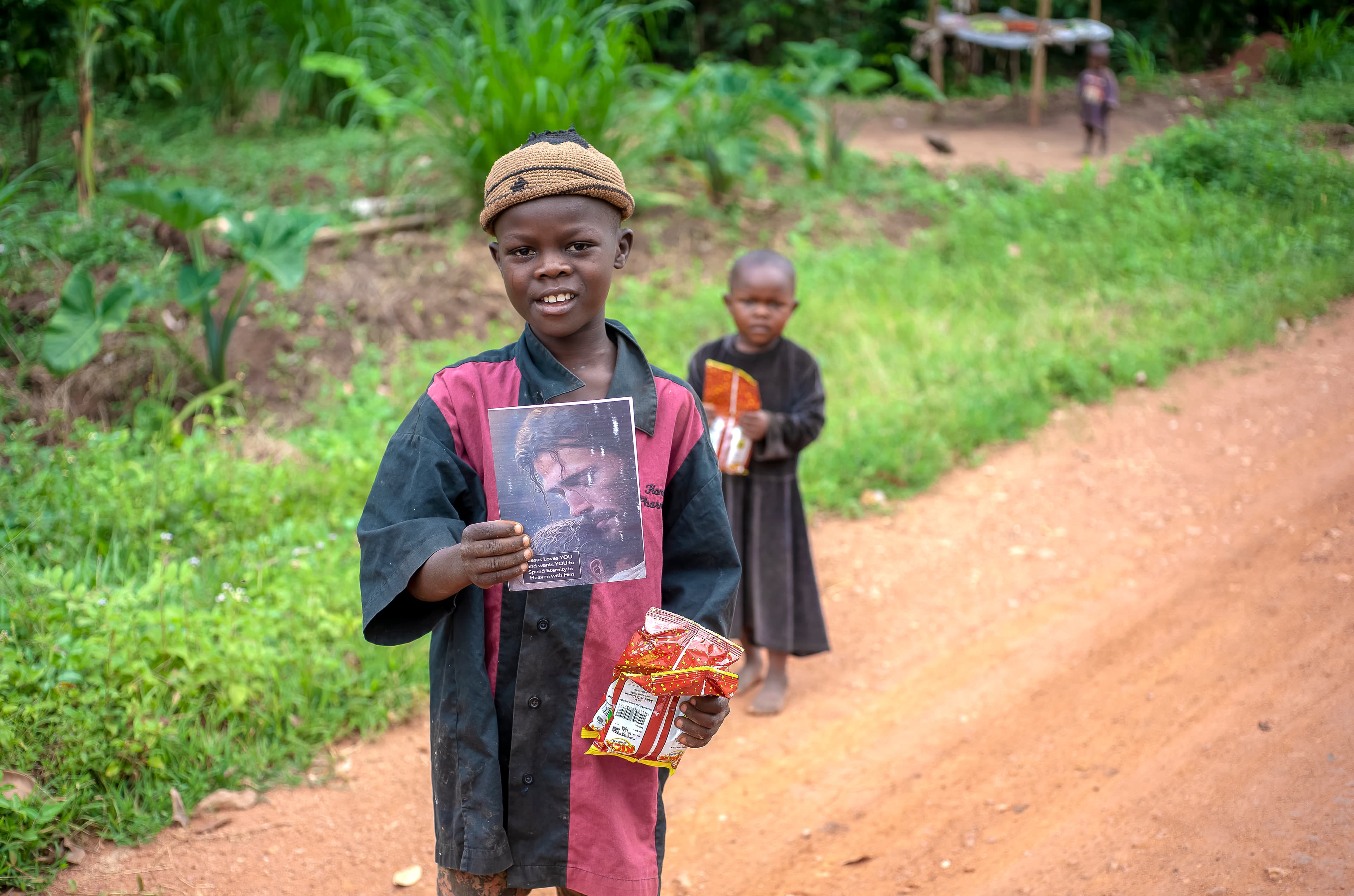 A man and child stand together outdoors holding a photo and food items.