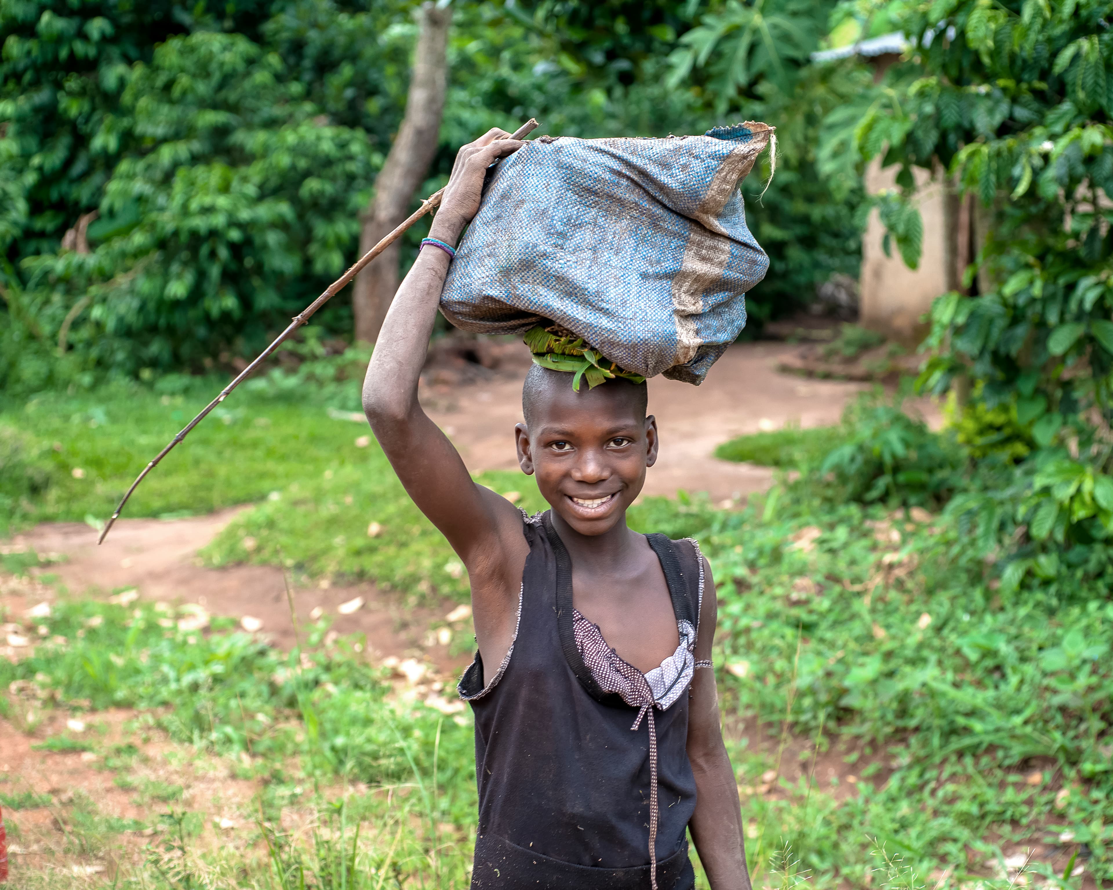 A boy smiles while carrying a bundle raised overhead outdoors.