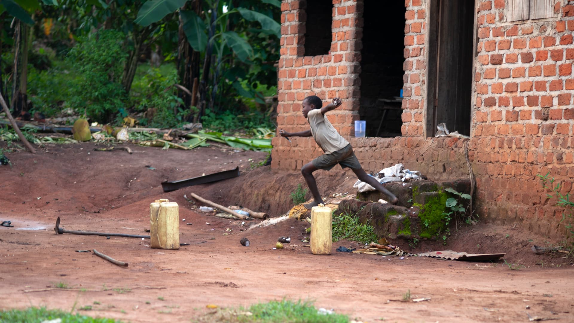 A partially collapsed brick building wall stands in an open dirt yard.